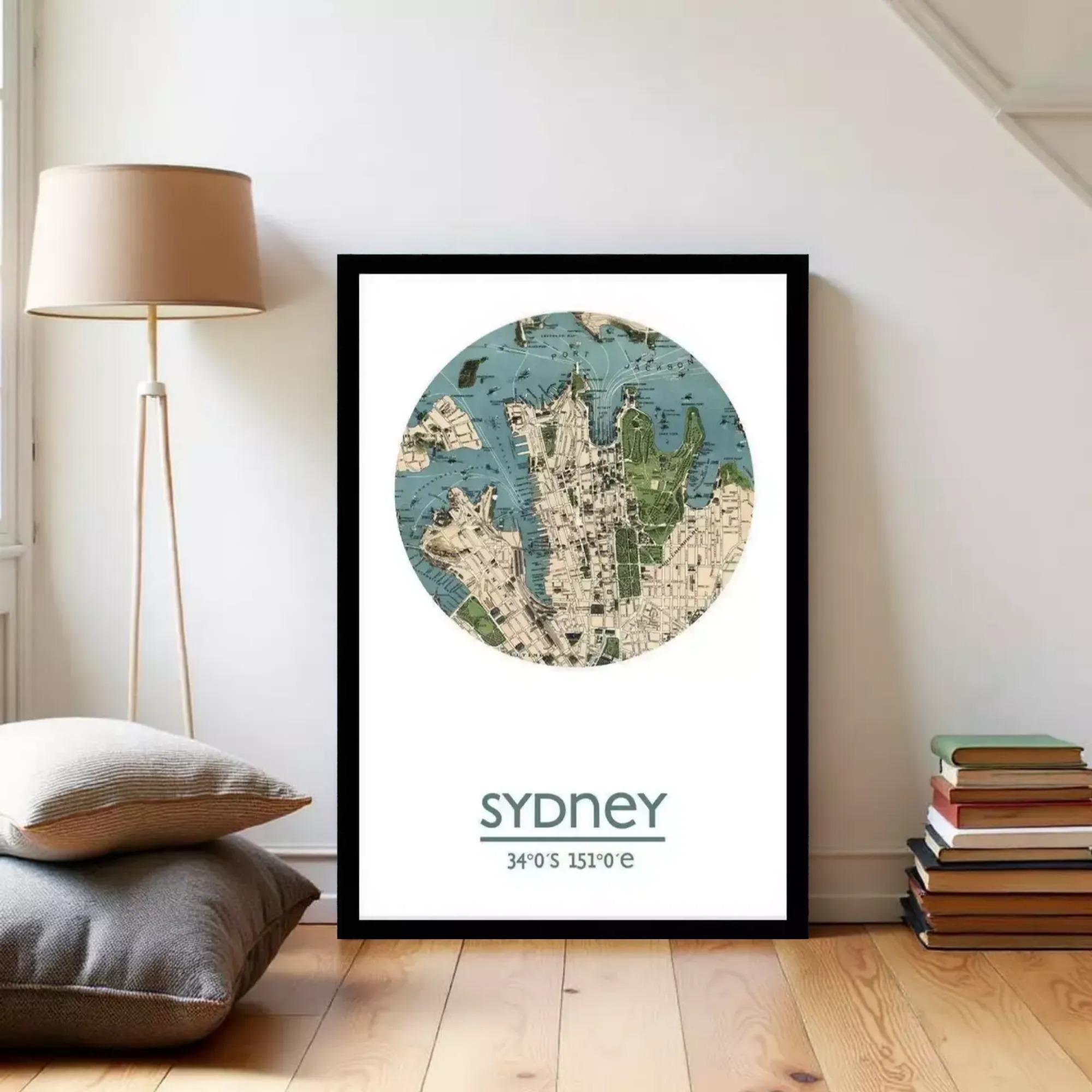 A framed map of Sydney, Australia, with the text "Sydney 34°S 151°E" printed on it, is displayed on a wall in a room with a lamp and books.
