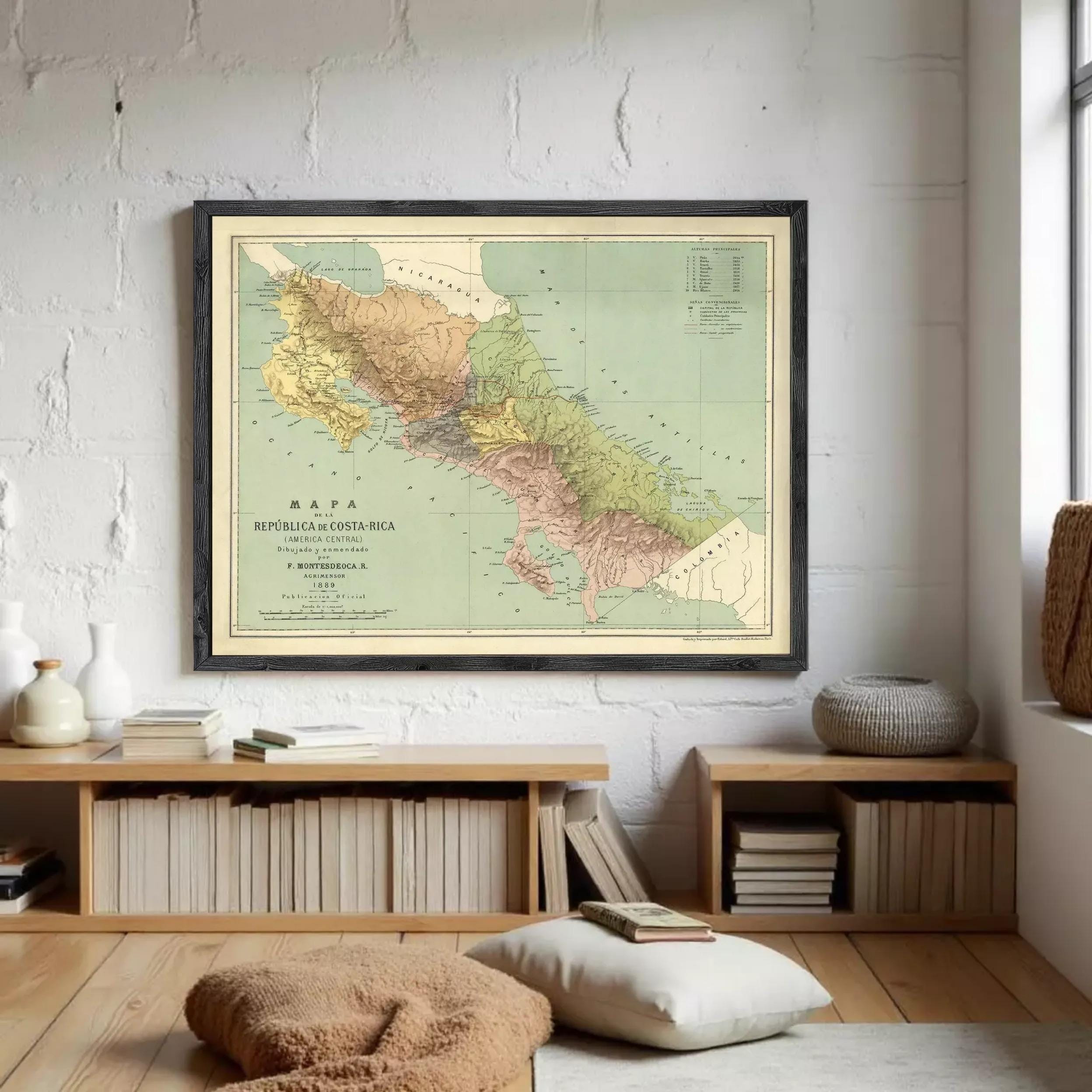 a framed map of Costa Rica hanging on a white wall in a room with a wooden floor and a bookshelf.