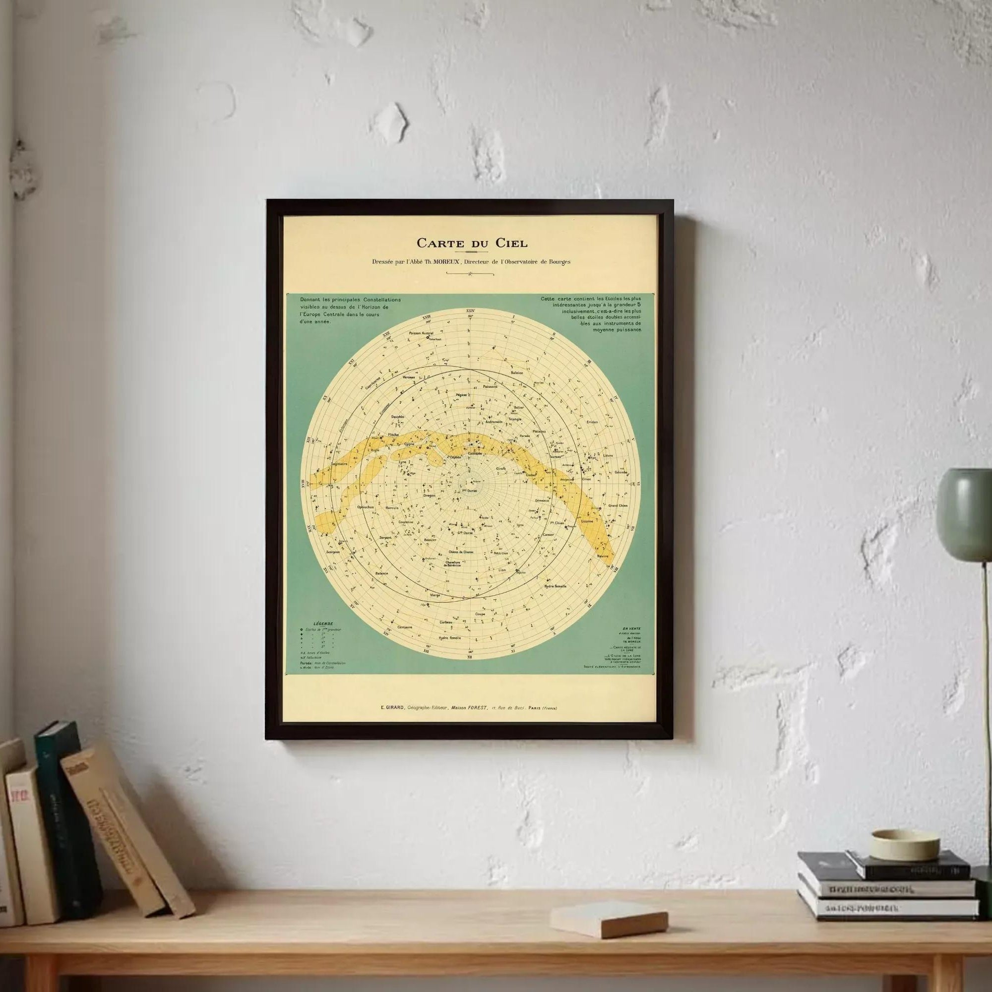 a framed vintage-style map of the night sky, hanging on a wall above a wooden desk with books and a lamp.
