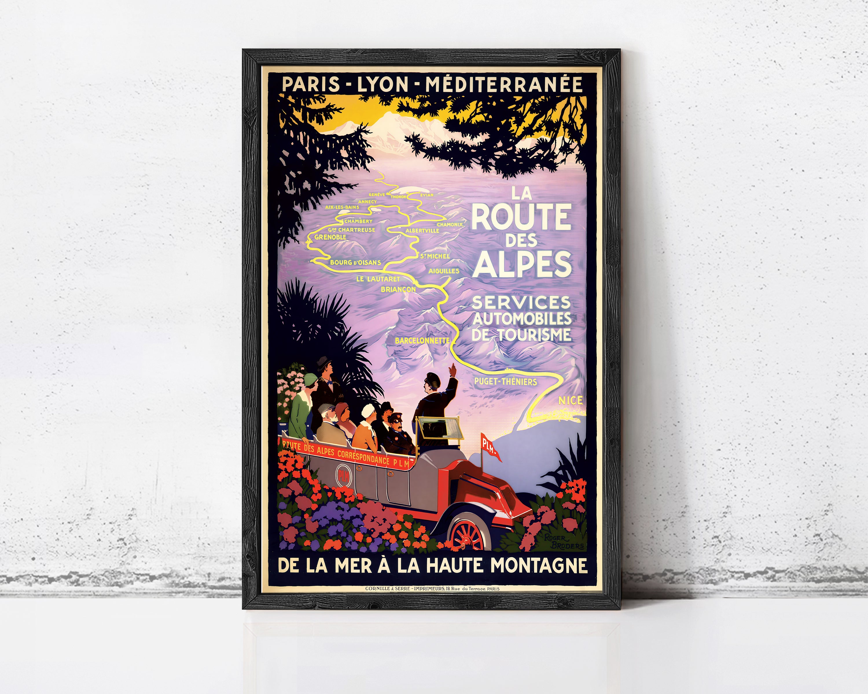 A framed vintage travel poster advertising a tour of the route to the Alps, featuring a car and people traveling through a scenic landscape.