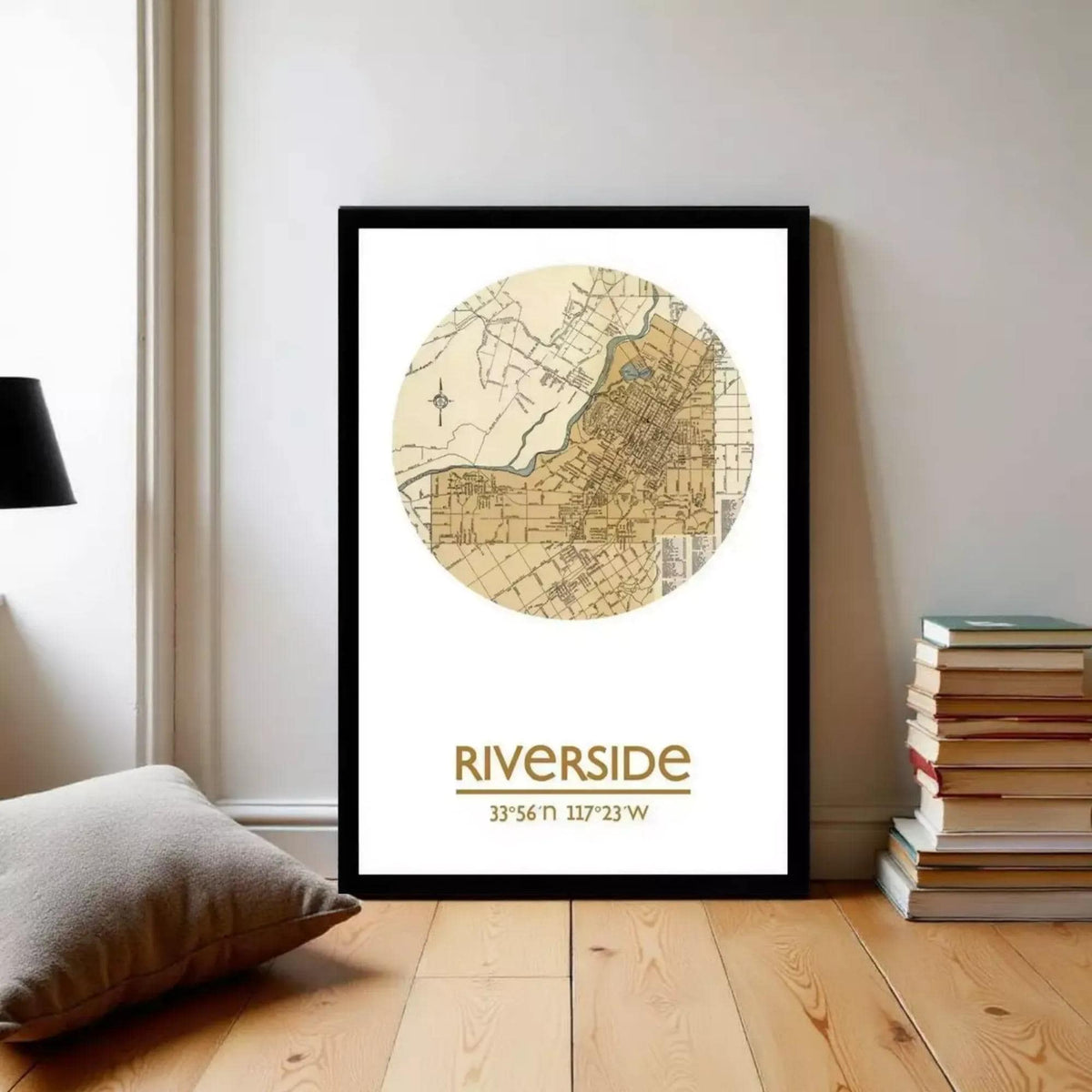 A framed map of the Riverside neighborhood, with a focus on the area around the river, is displayed on a wall in a room with a stack of books and a pillow.