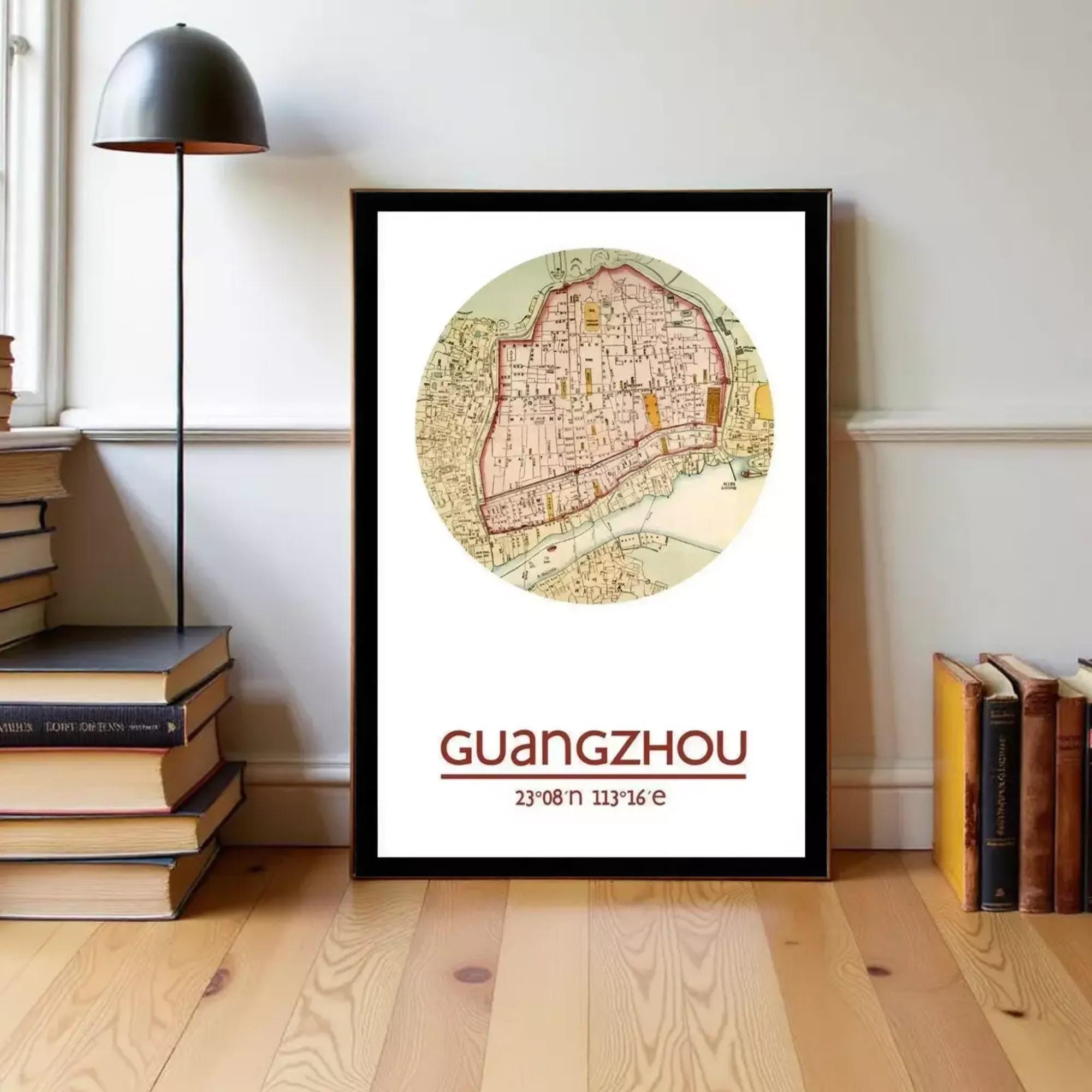 A framed map of Guangzhou, China, with the text "GUANGZHOU" and the date "23/09/13" printed on it, is displayed on a wooden floor next to a stack of books.