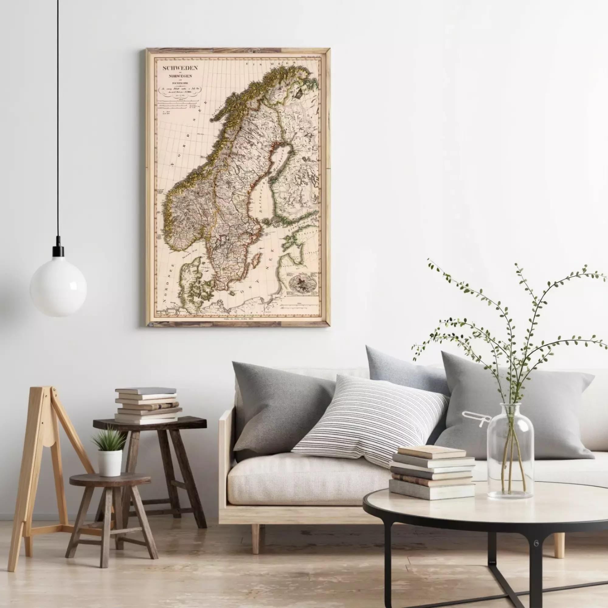 a living room with a large map of Europe hanging on the wall, a wooden stool, a round coffee table with books and a plant, and a gray couch with pillows.