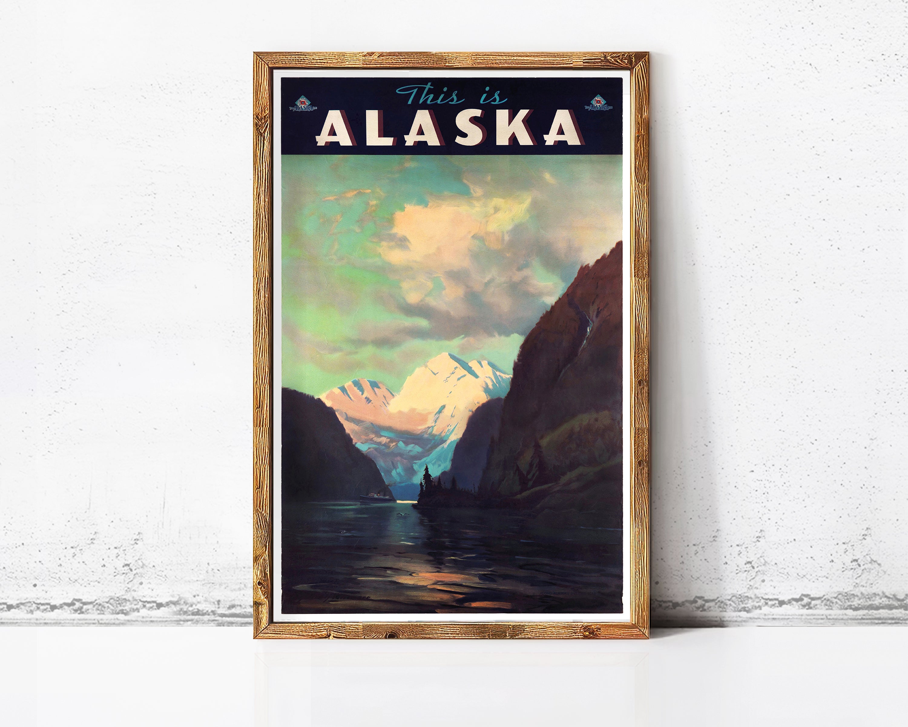 The image is a framed vintage travel poster depicting a scenic landscape with mountains, water, and clouds, with the text "This is Alaska" prominently displayed.