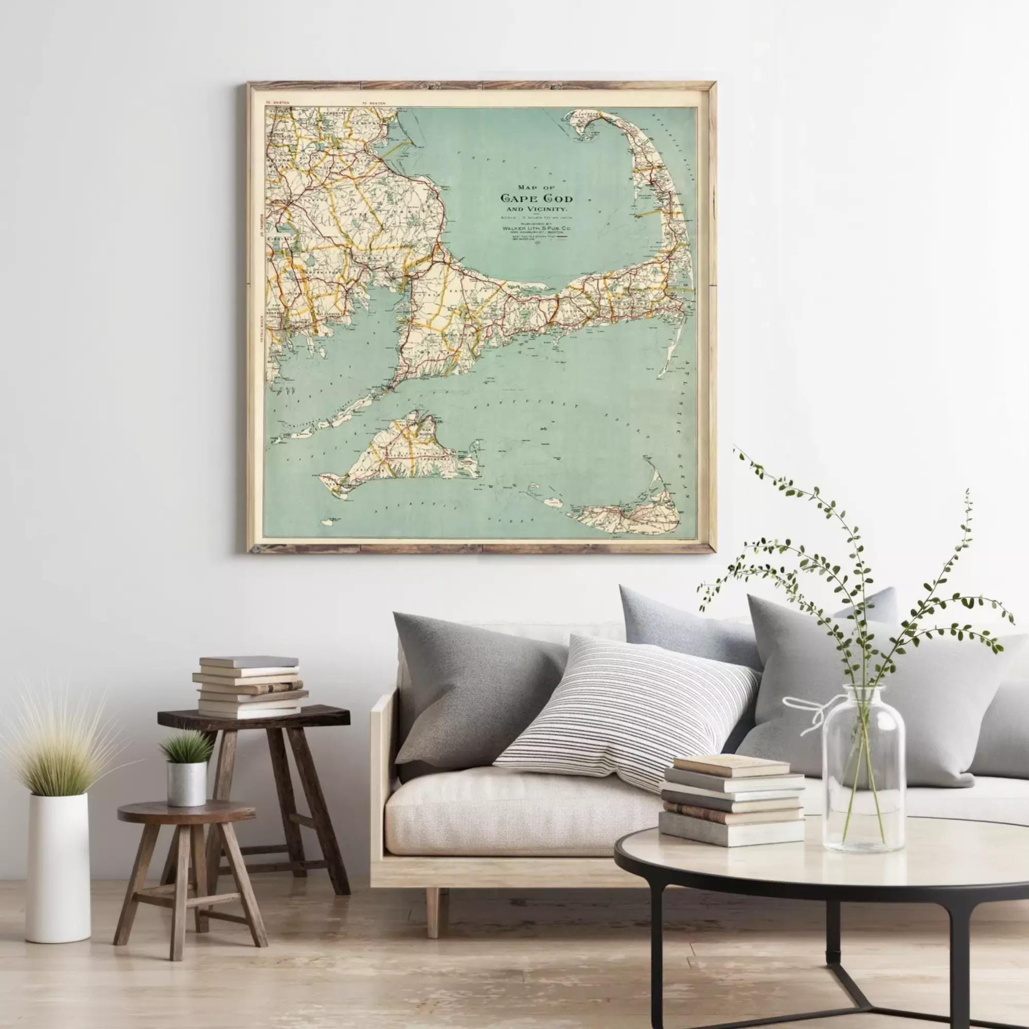 a living room with a large framed map of Cape Cod hanging on the wall above a couch with pillows. There are also some books and decorative items on the couch and table below the map.
