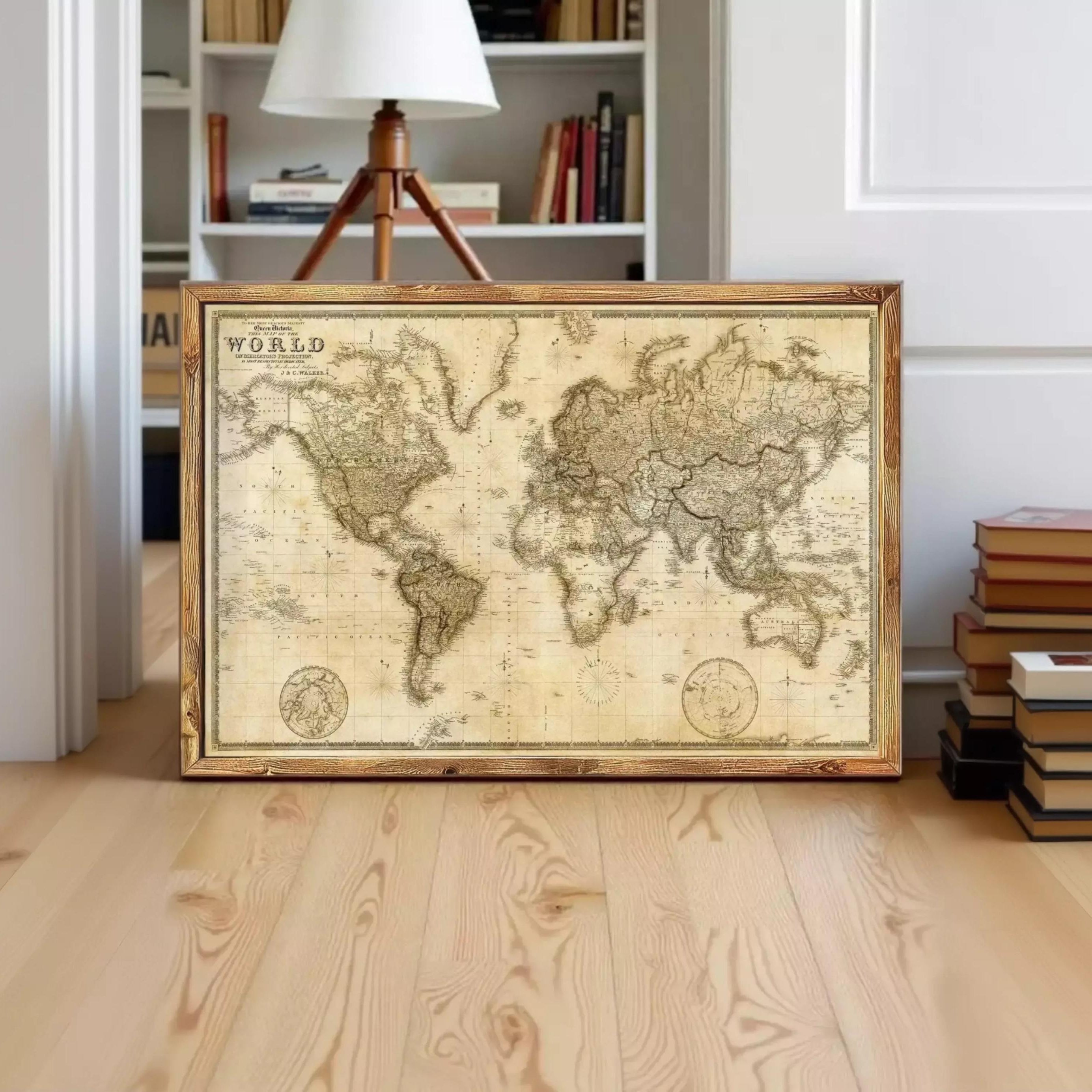 A framed antique world map is displayed on a wooden floor in a room with a bookshelf in the background.