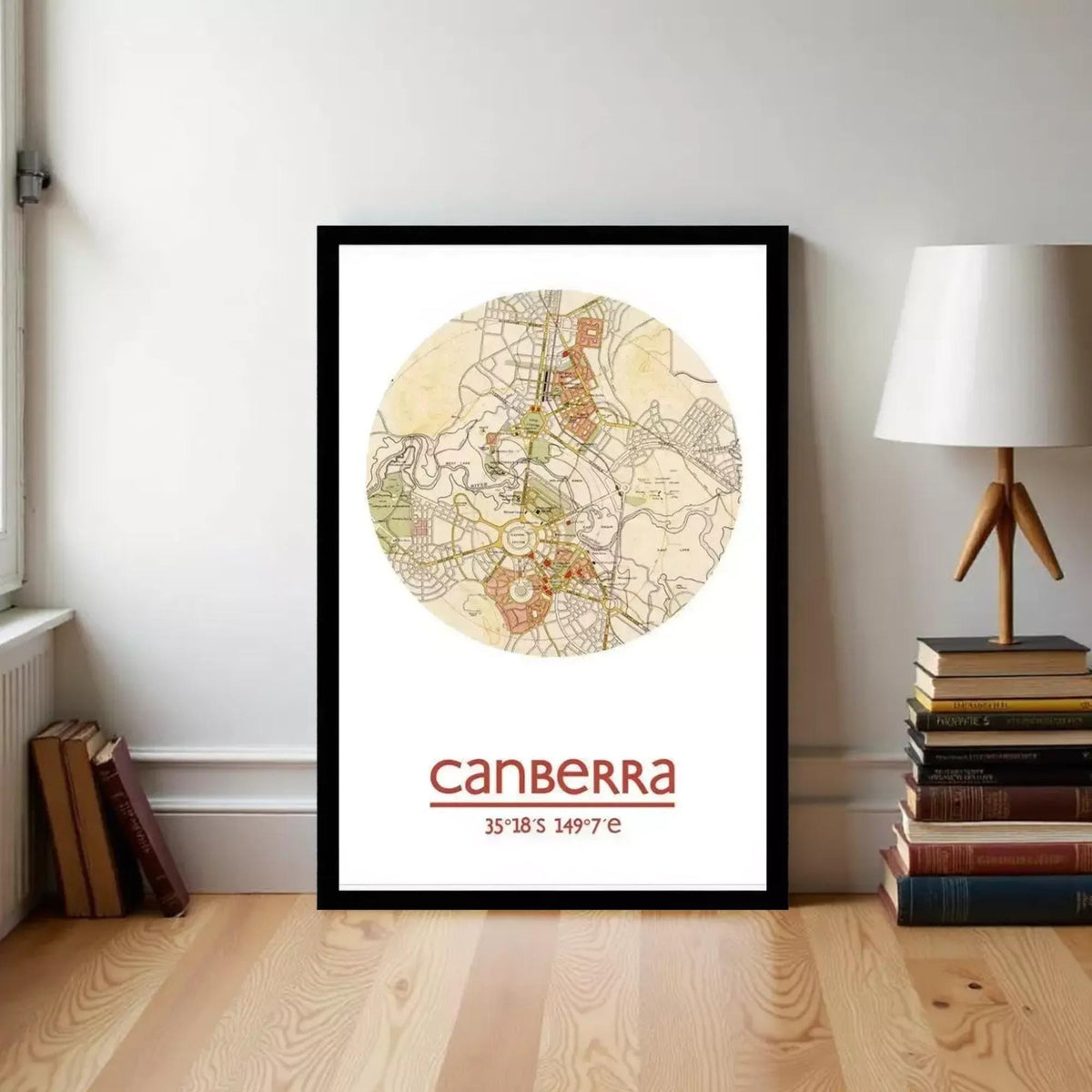 A framed map of Australia with the city of Melbourne highlighted, placed on a wooden floor next to a stack of books and a lamp.