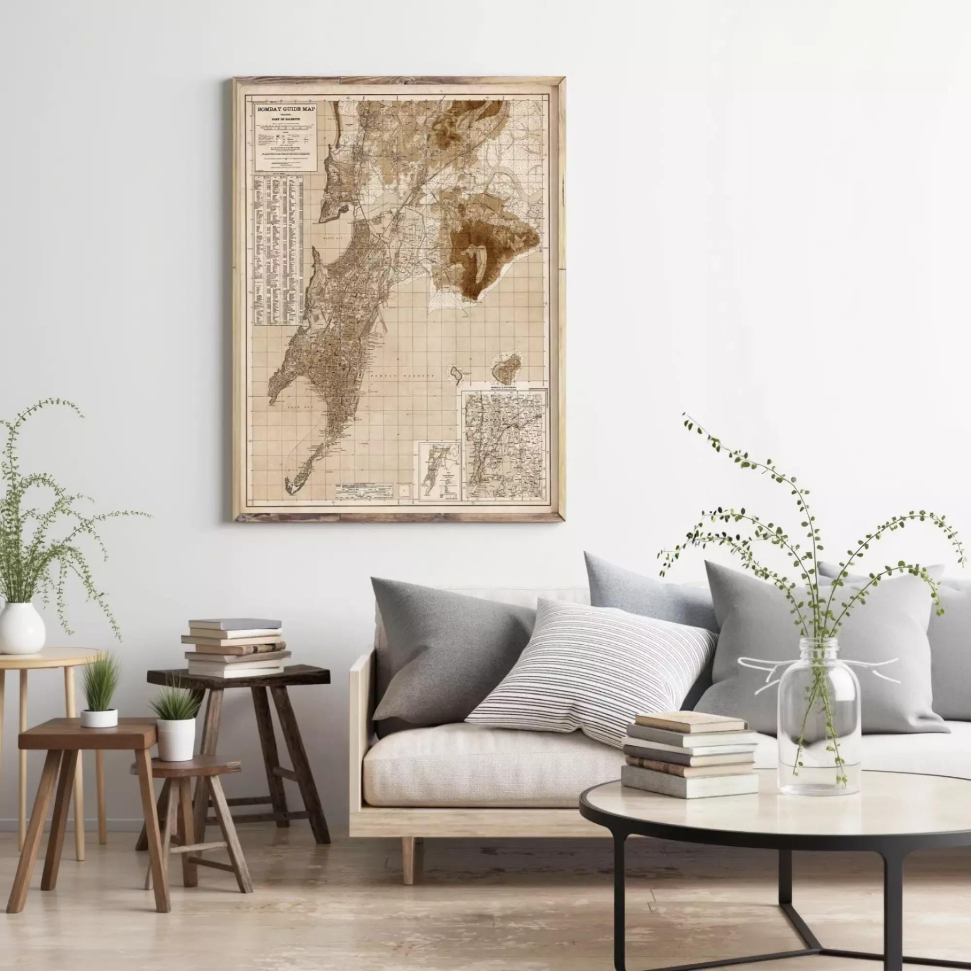 a living room with a large framed map hanging on the wall above a gray sofa with striped pillows. The room has a wooden coffee table, a side table with a plant, and a bookshelf with several books.