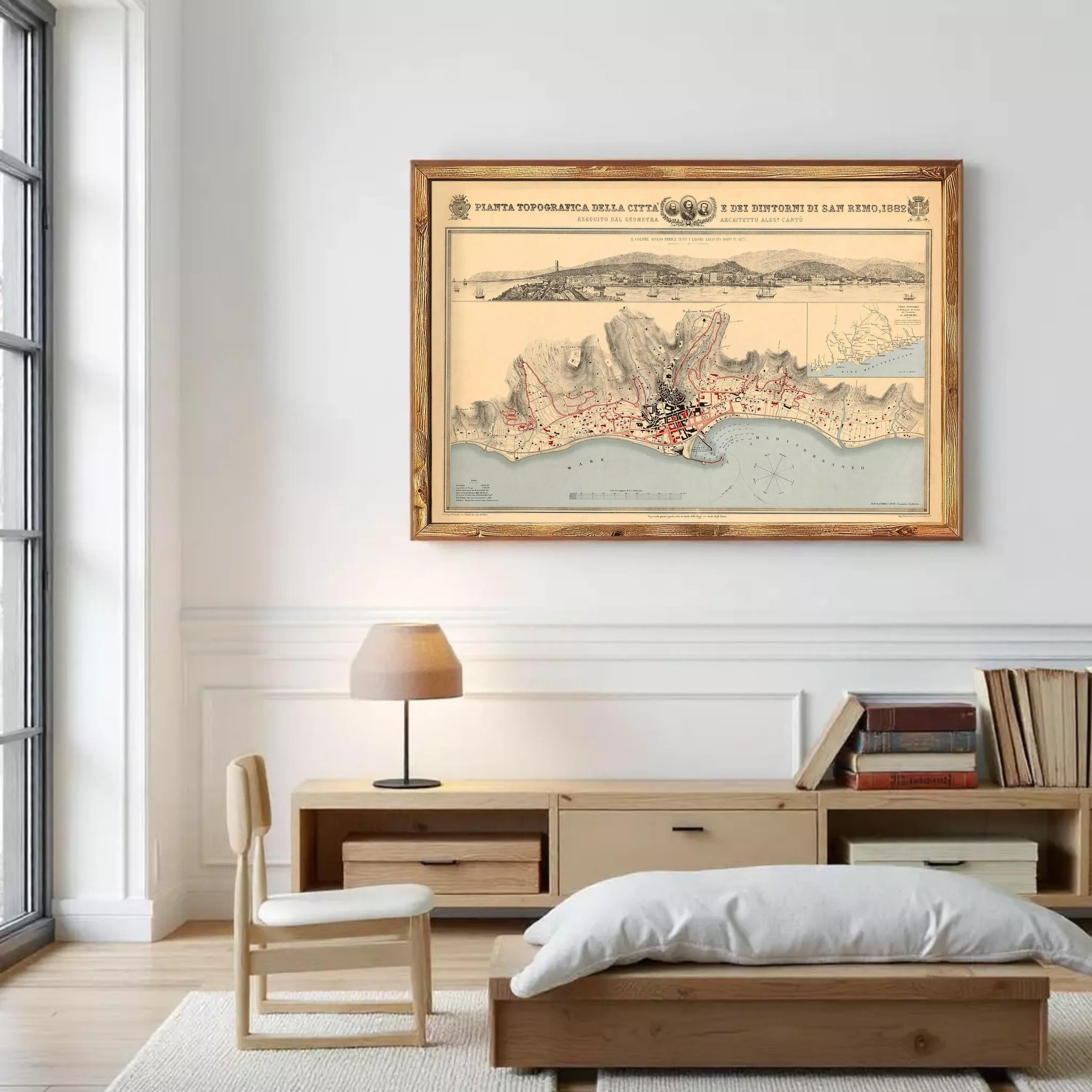 a framed map of a city hanging on a wall in a room with a wooden table, chair, and bookshelf below it.