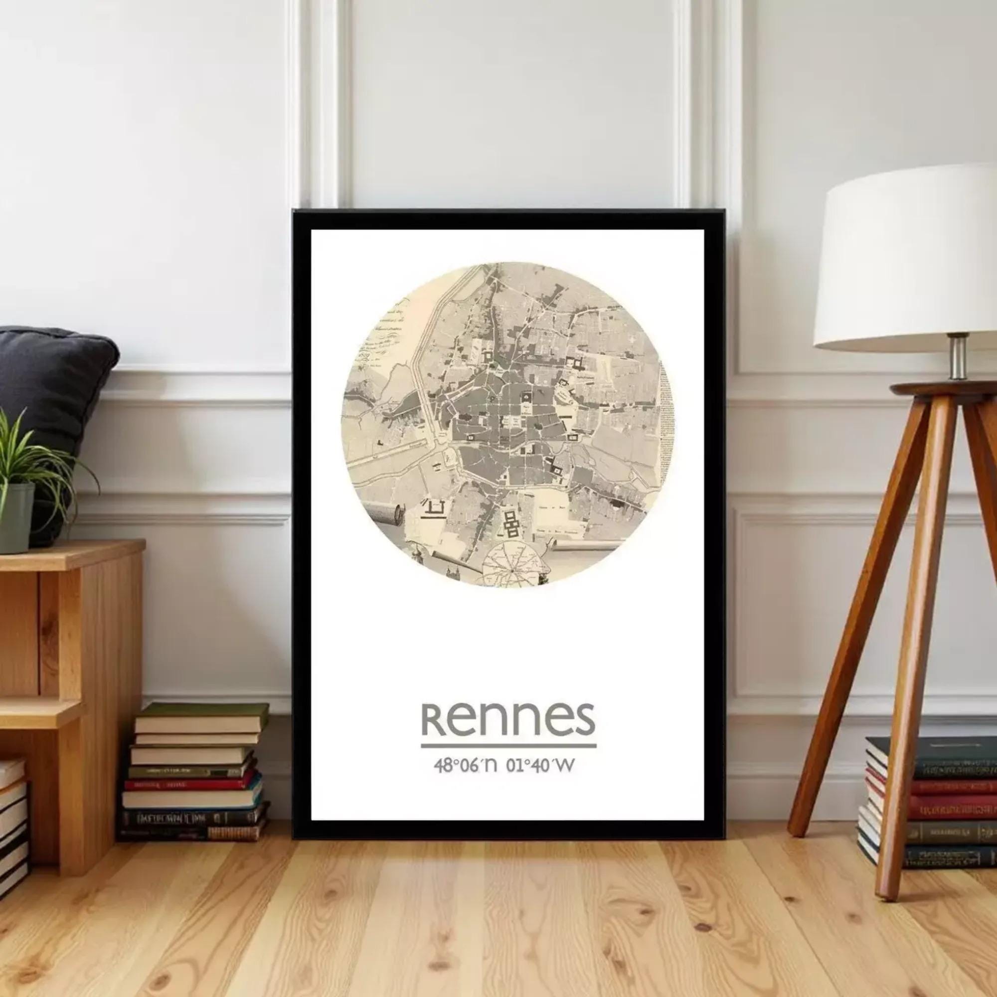 A framed map of Rennes, a city in France, is displayed on a wall in a room with a wooden floor and a lamp.