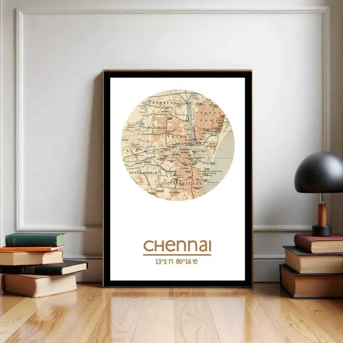 A framed map of the city of Chennai, India, with the text "Chennai" and "13th & 16th" printed on it, is displayed on a wall next to a stack of books and a lamp.