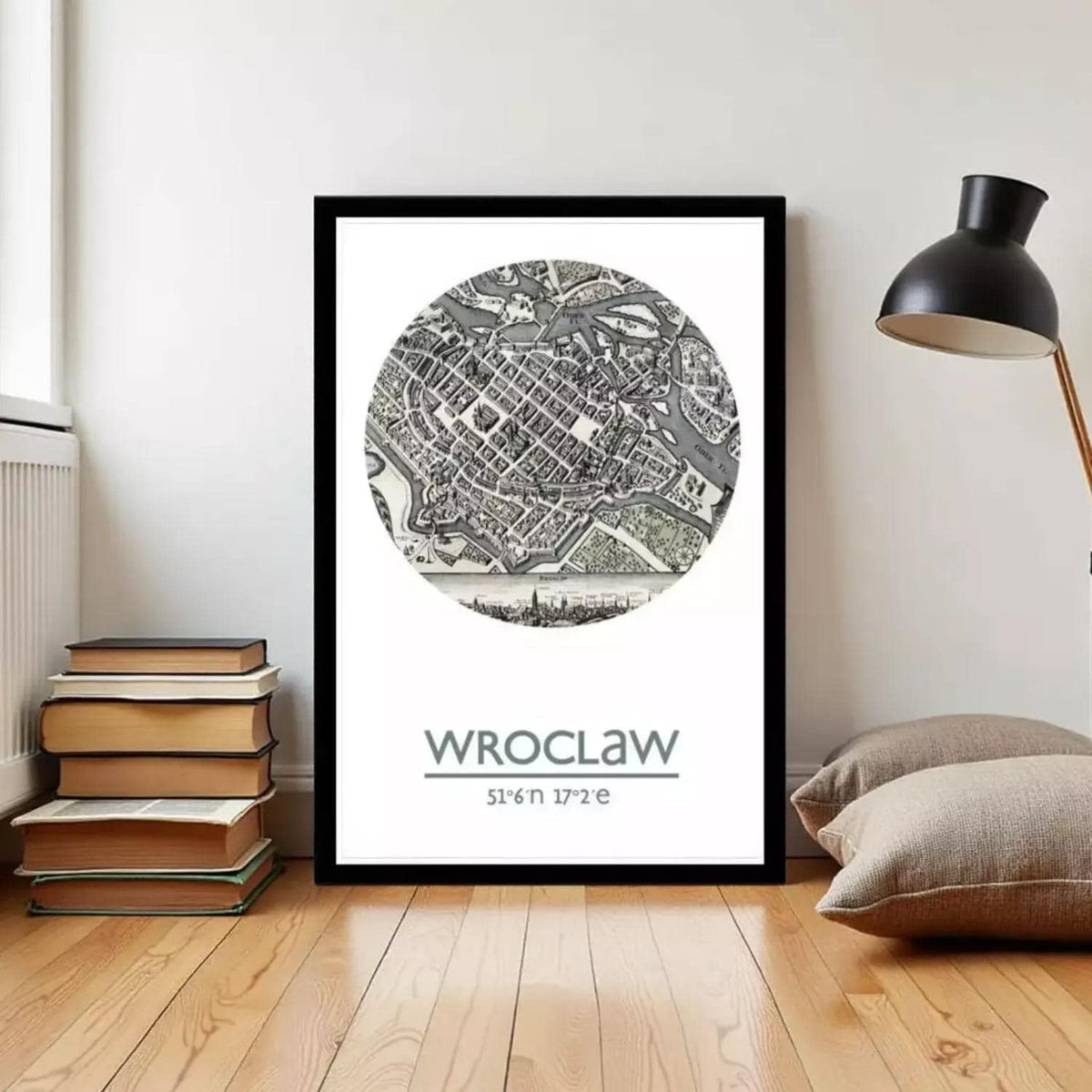 A framed poster of a map of Wrocław, Poland, displayed on a wall in a room with a stack of books and a lamp.