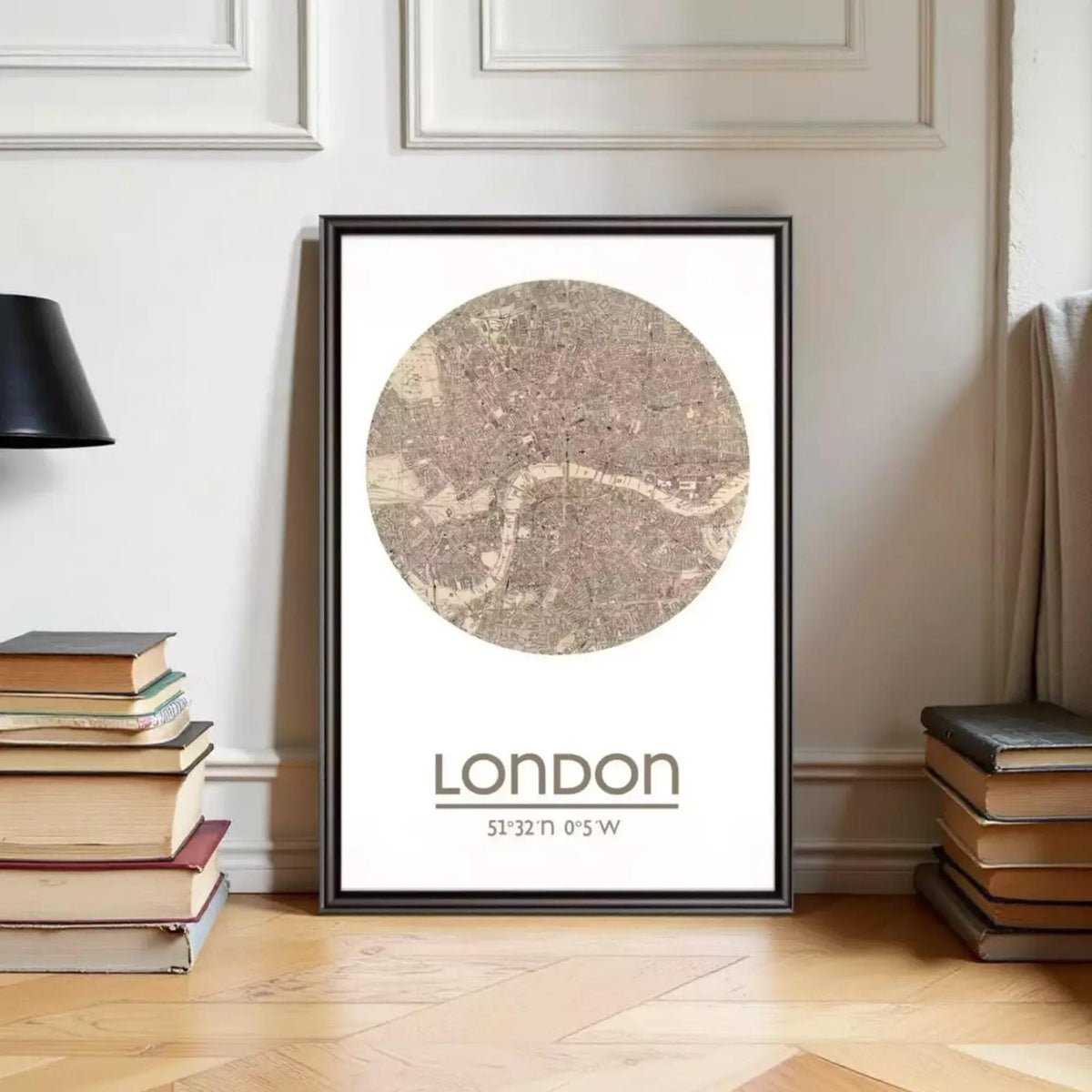 A framed map of London with the text "LONDON 51°32'N 0°57'W" printed on it, placed on a wooden floor next to a stack of books.