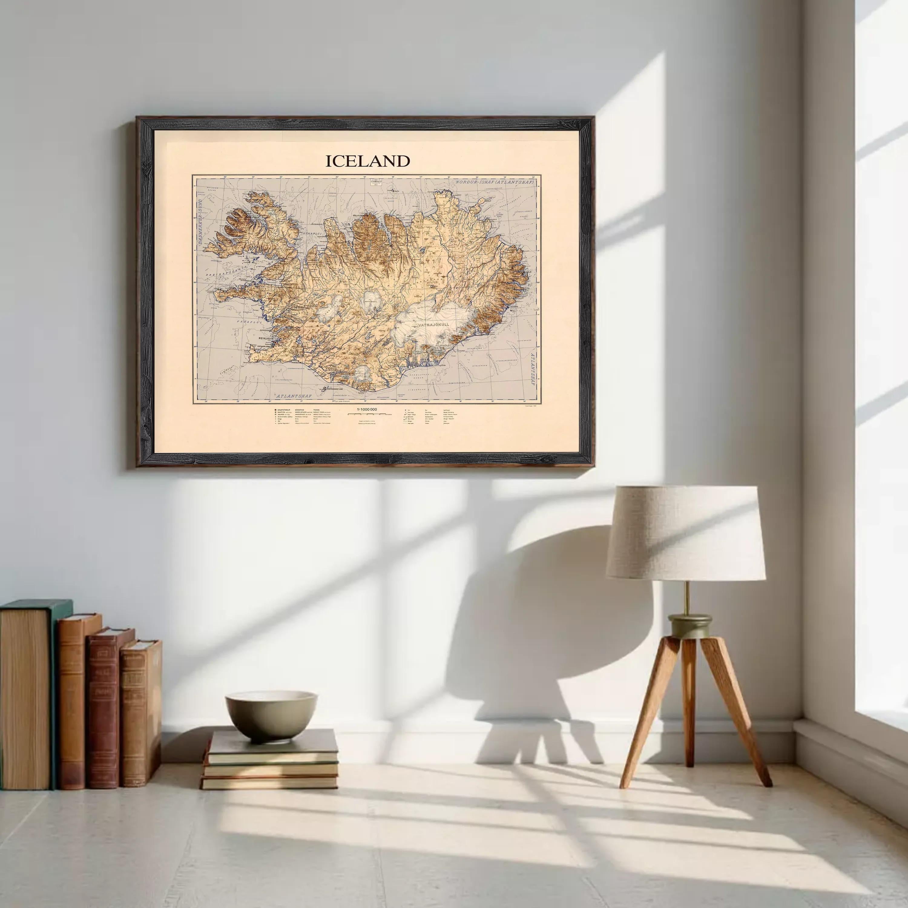 a framed map of Iceland hanging on a wall, with a lamp and a stack of books placed nearby.