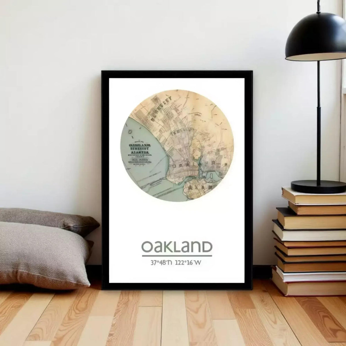 A framed map of Oakland, California, with the text " Oakland 37°48' 12.16 W" printed on it, is displayed on a wall next to a stack of books and a lamp.