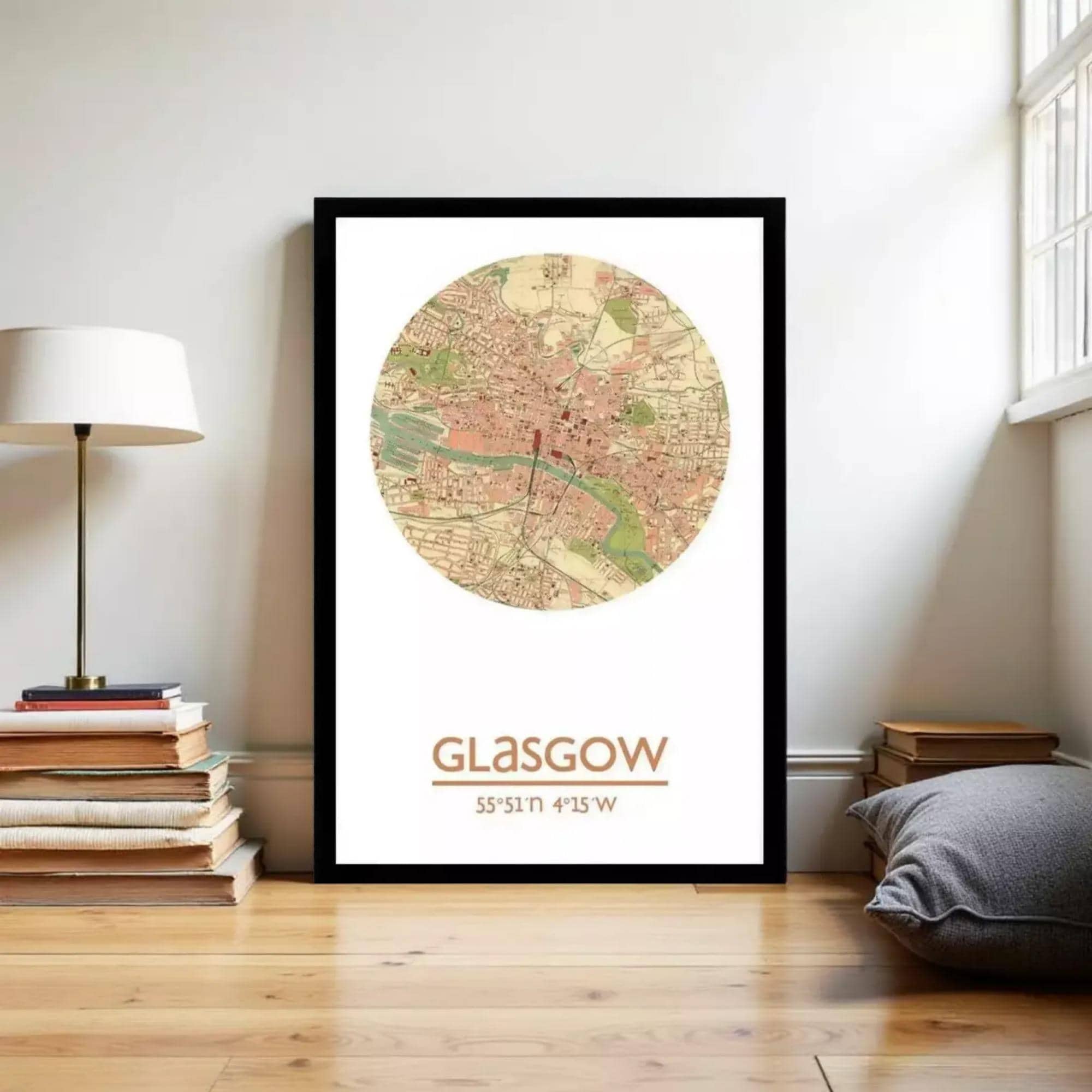A framed map of Glasgow, Scotland, with the city's location and surrounding areas, is displayed on a wall in a room with a lamp and books.