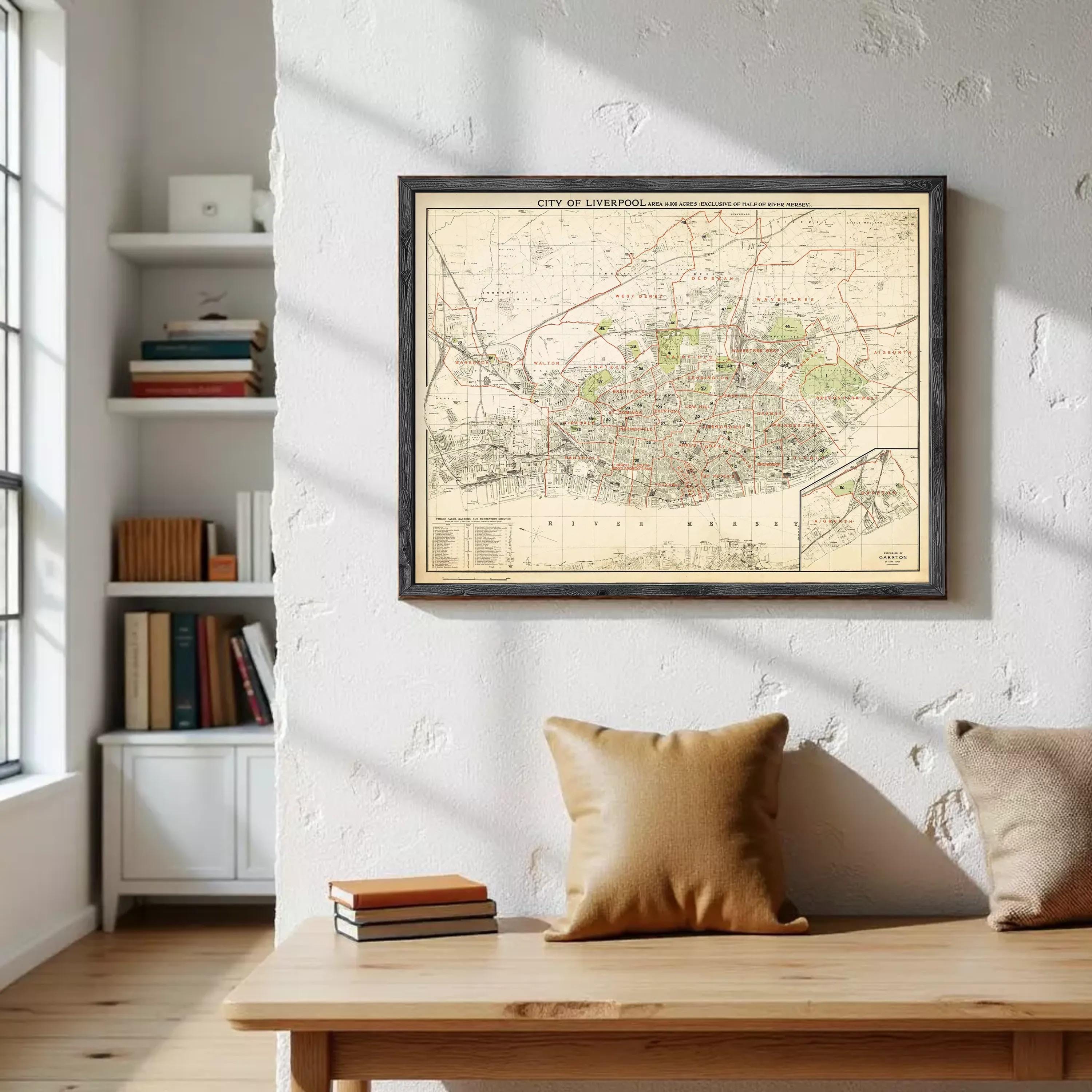 a wooden table with a stack of books and a brown pillow on it, and a framed map of Liverpool hanging on the wall above the table.