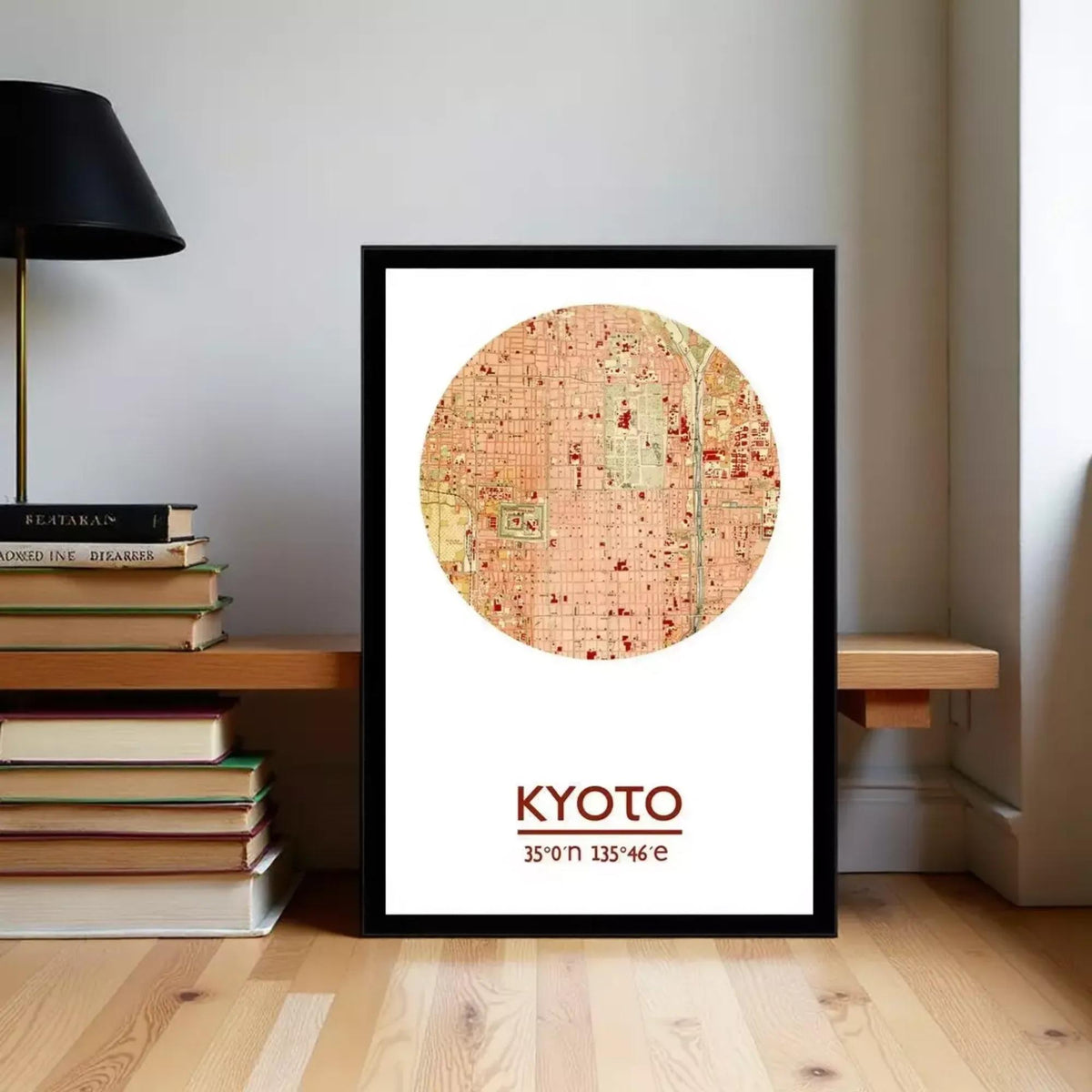 A framed map of Kyoto, Japan, with the city's name and location printed on it, is displayed on a wooden floor next to a stack of books.