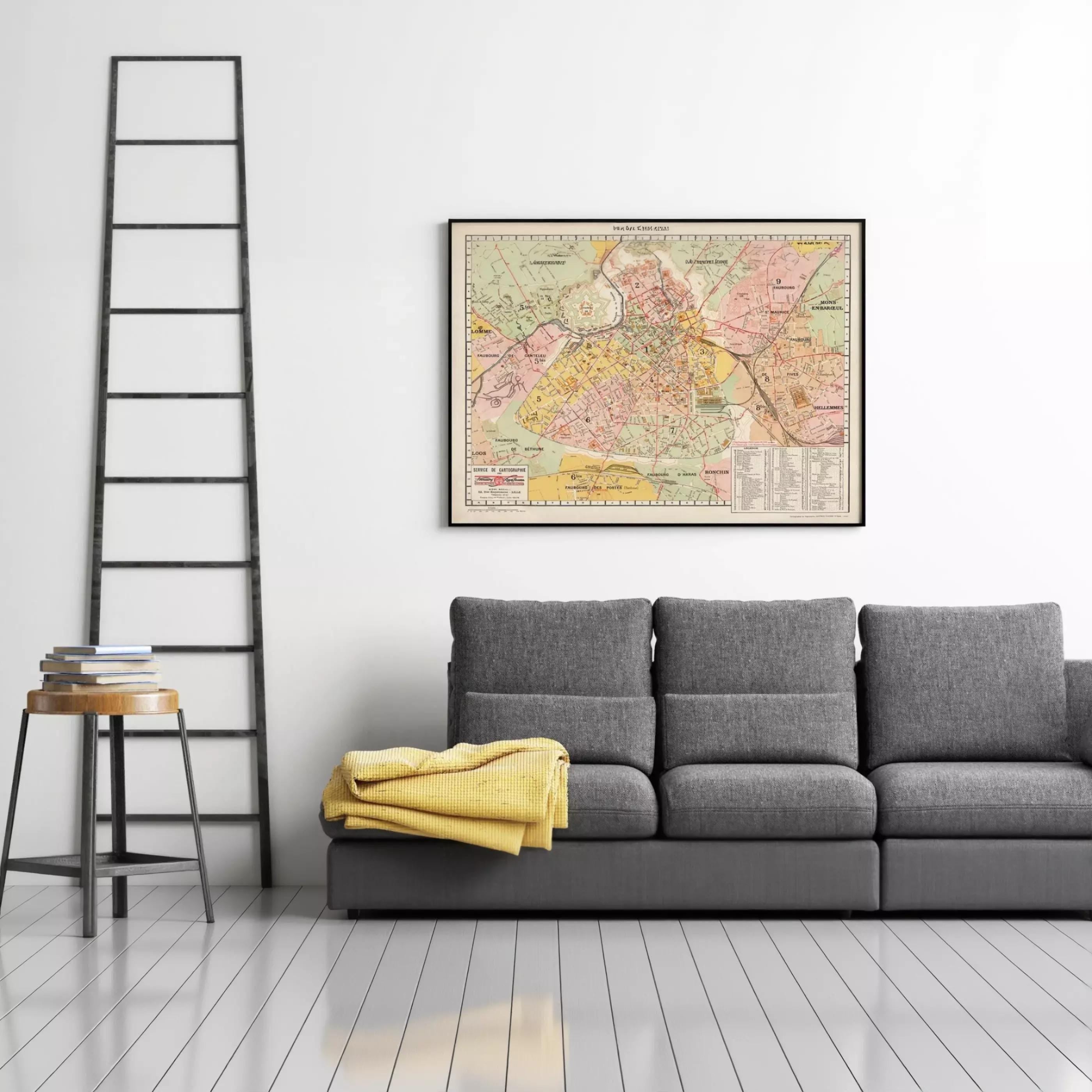 a gray sofa with a yellow blanket draped over it, and a framed map of Paris hanging on the wall above the sofa.