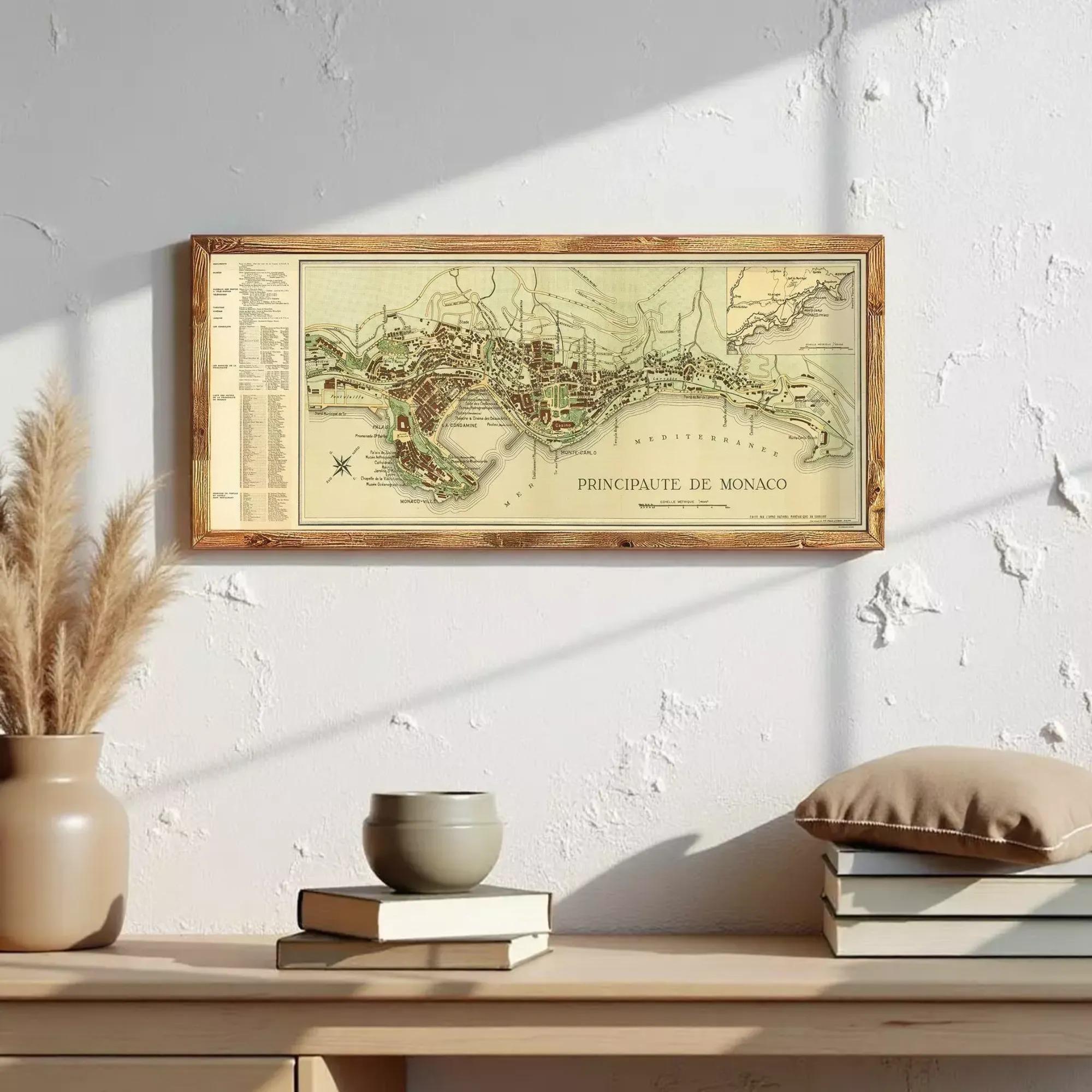 a framed map of Monaco hanging on a wall above a wooden shelf with books and a vase.