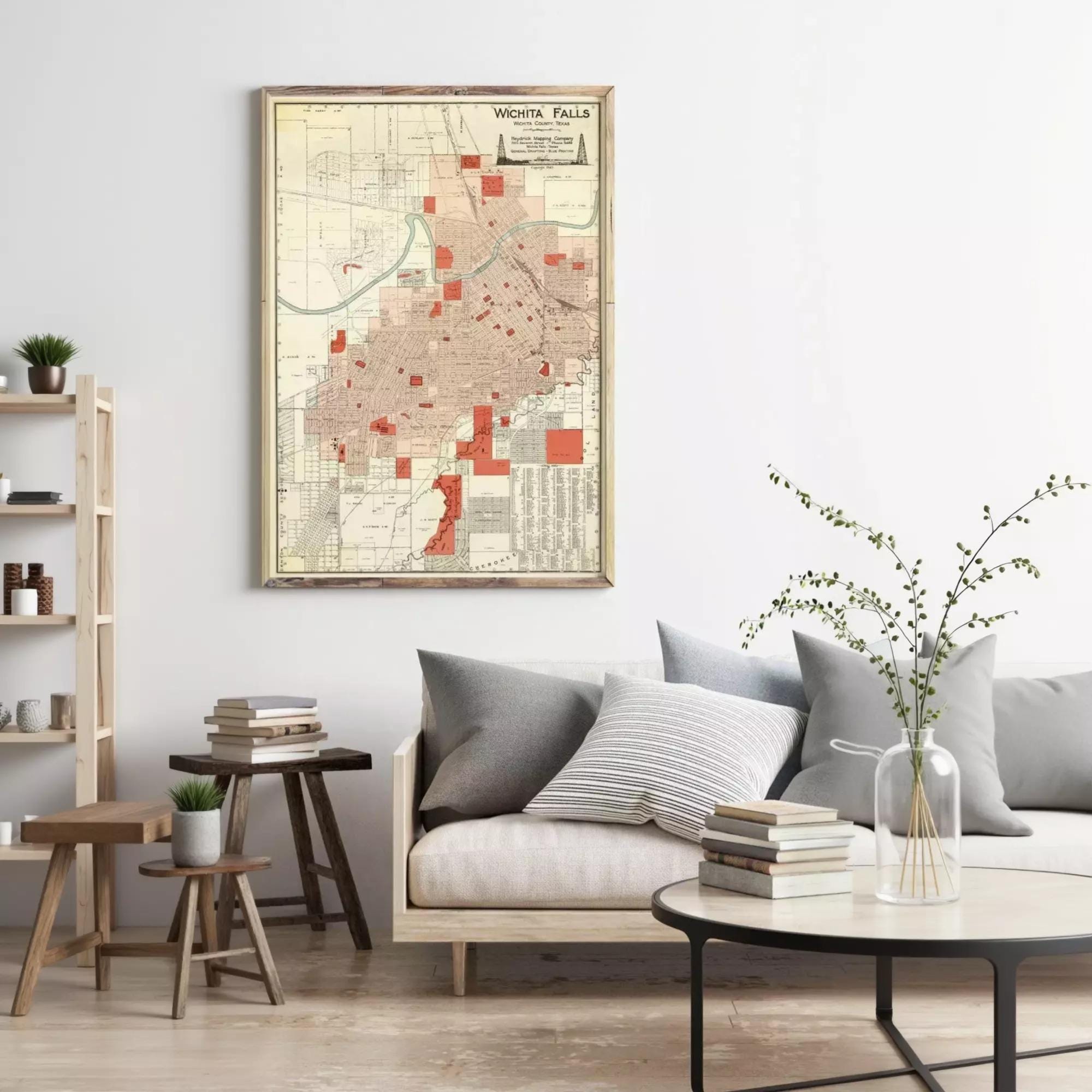 a living room with a large framed map of the city of Spokane, Washington, hanging on the wall. The room has a gray couch, a coffee table with books and a vase of flowers, and a wooden bookshelf.