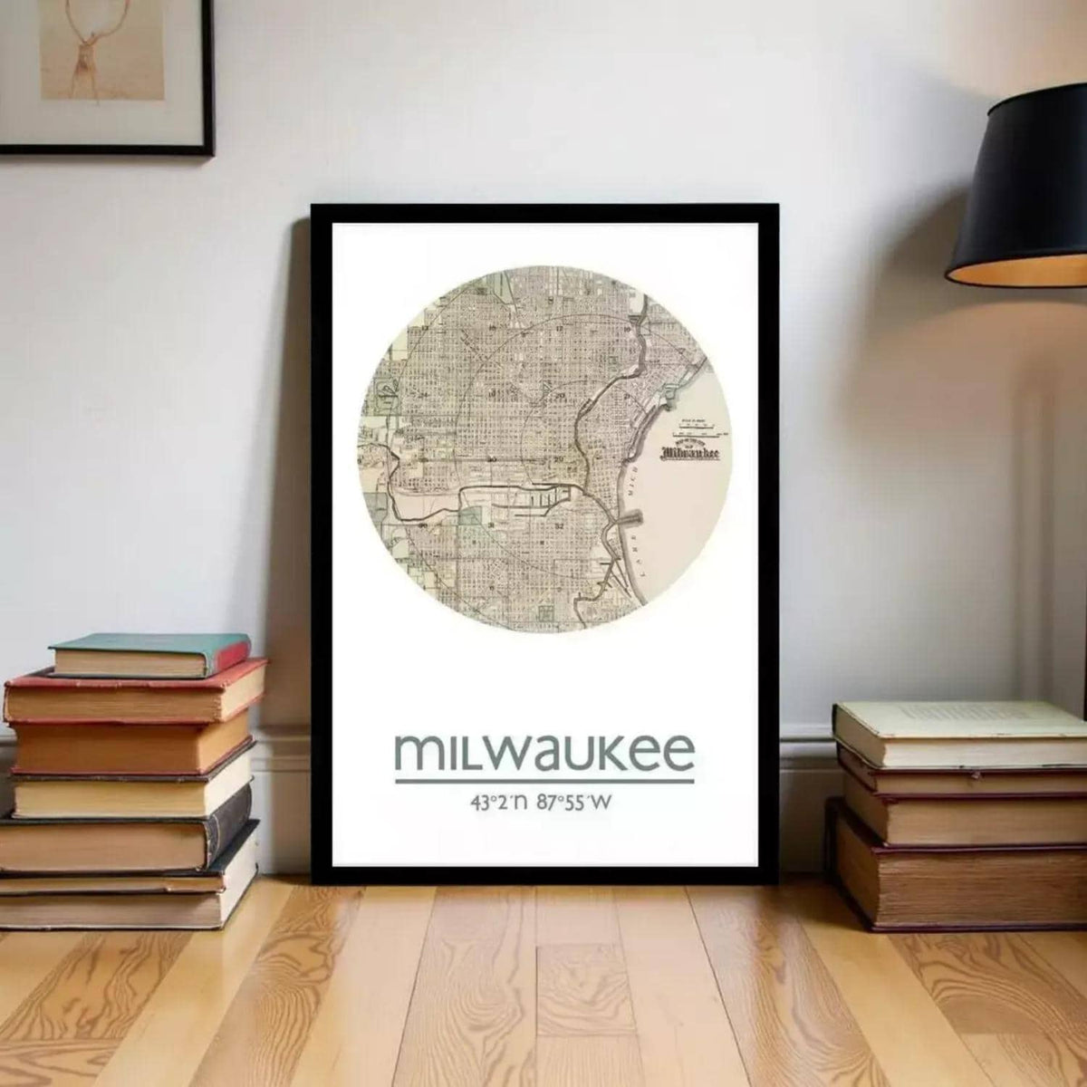 A framed map of Milwaukee, Wisconsin, with the city's name and coordinates displayed, is placed on a wooden floor next to a stack of books.