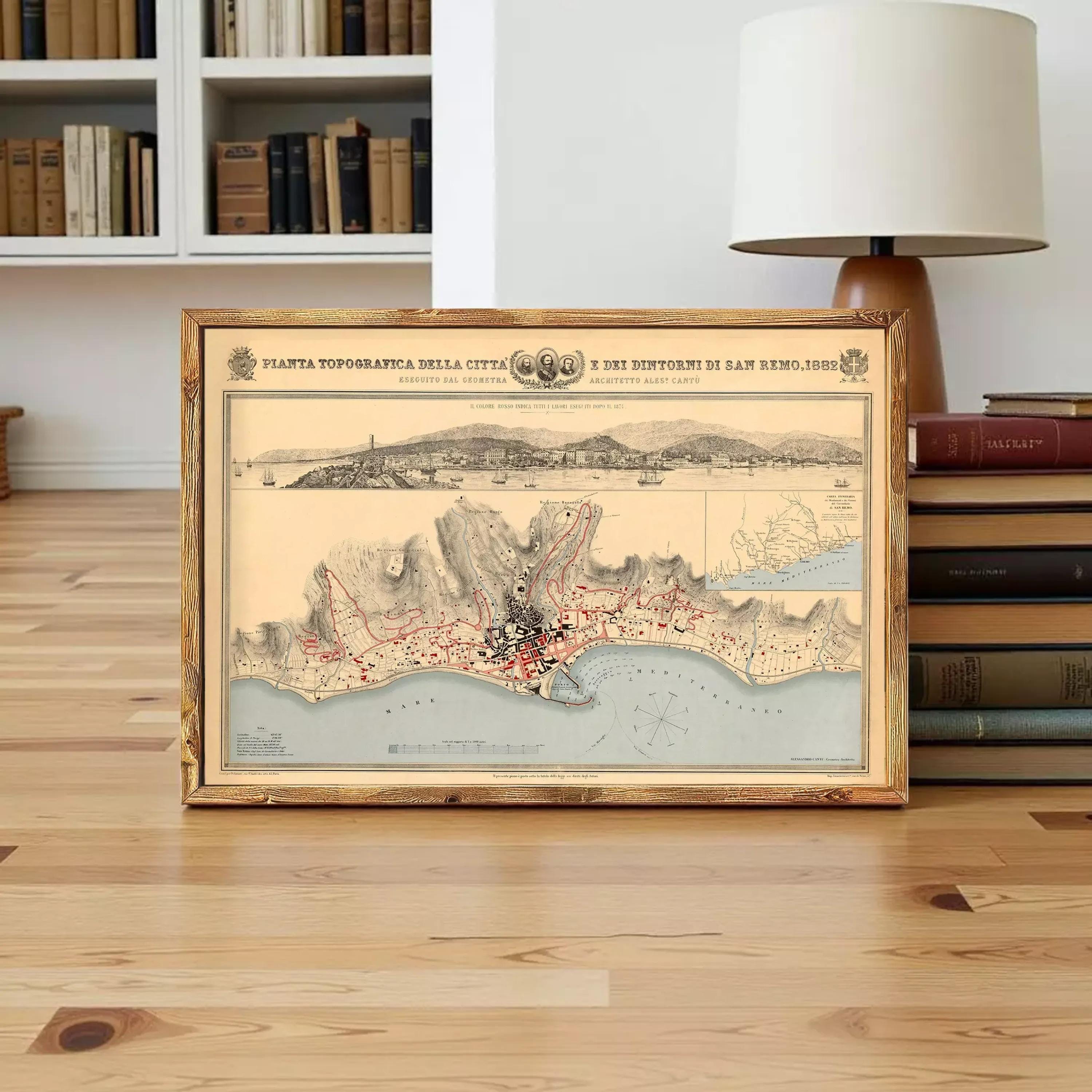 a framed map of a coastal city, with a bookshelf and a lamp in the background.