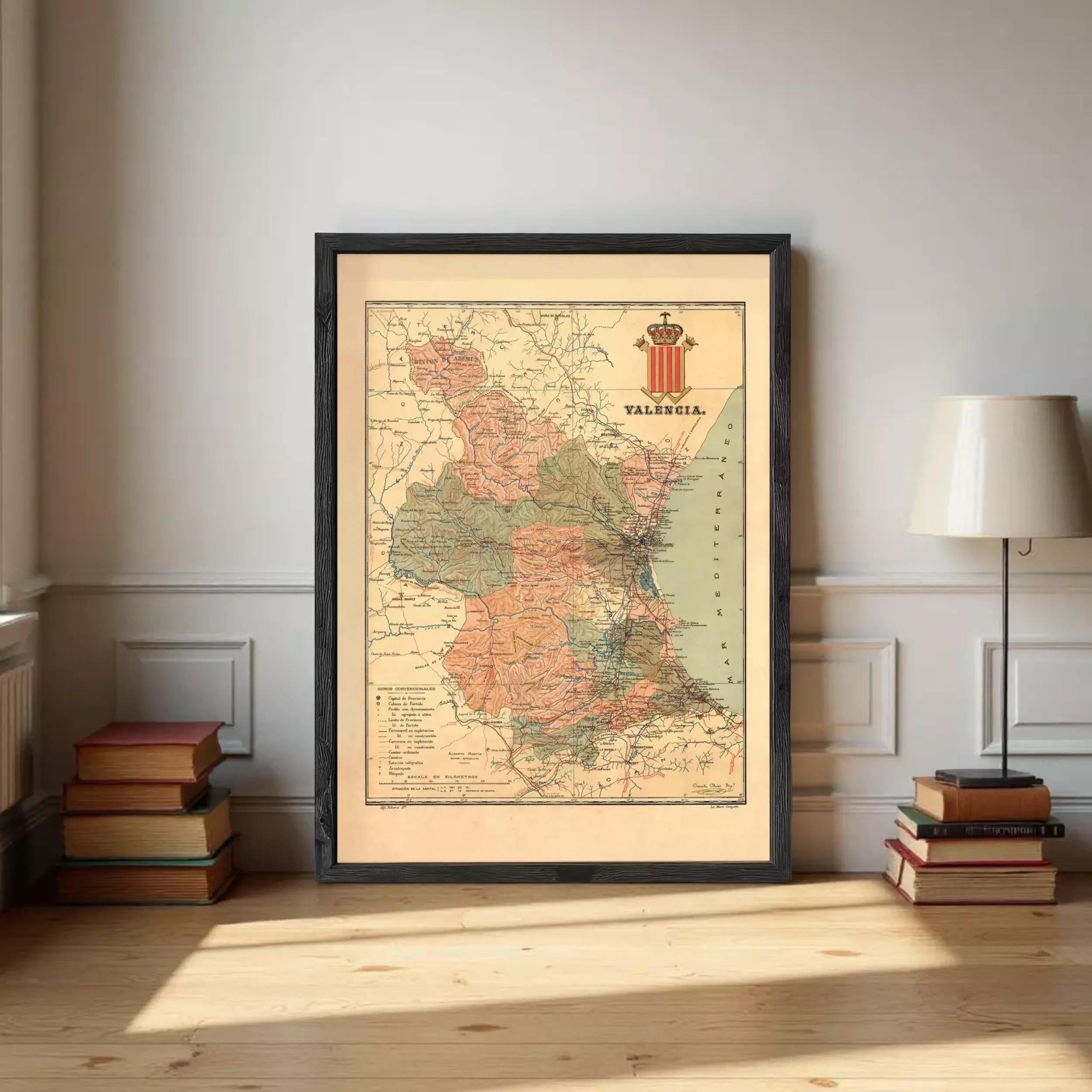 a framed map of the region of Valence, with a lamp and a stack of books on either side of it.