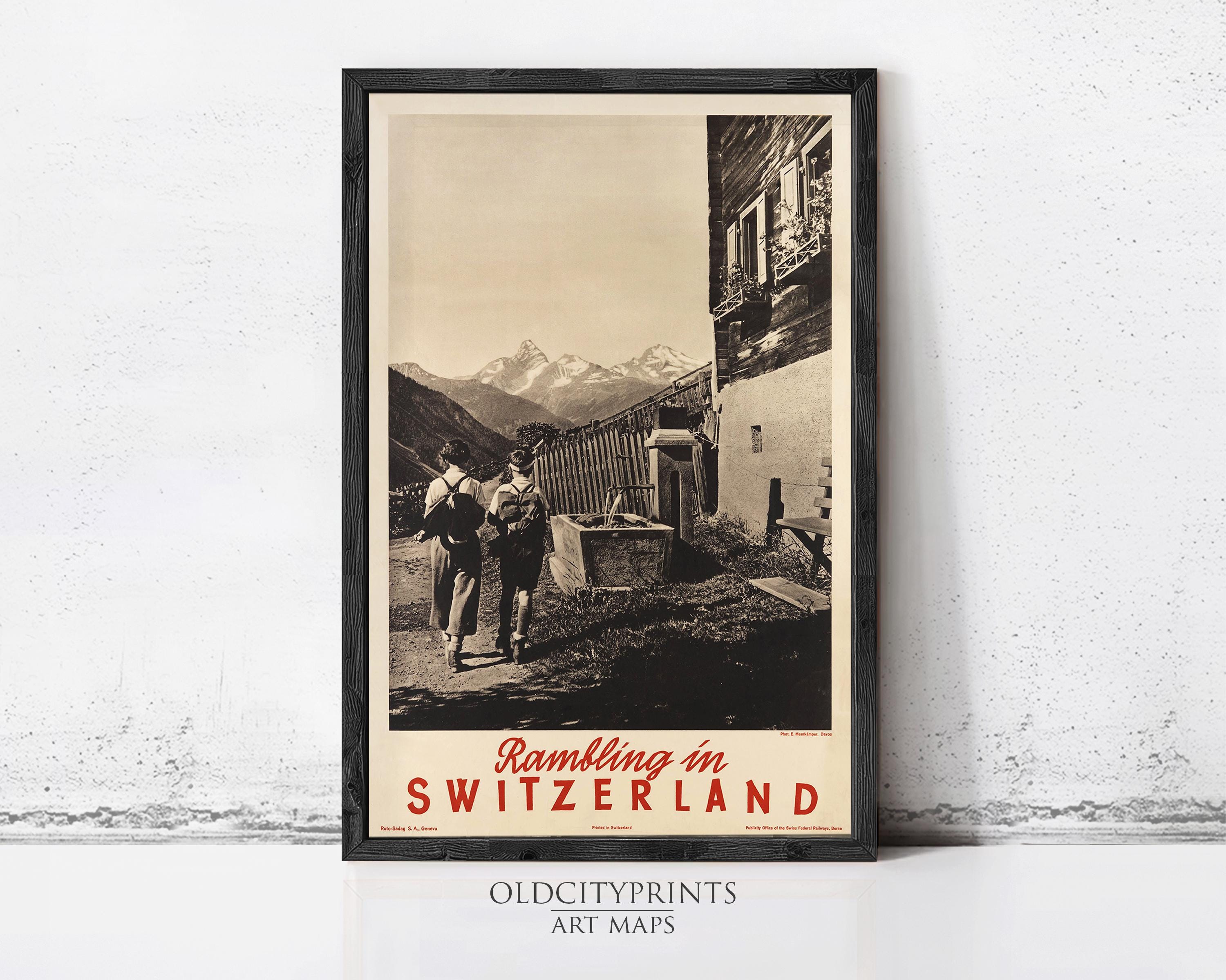 A framed vintage travel poster depicting a scenic mountain landscape in Switzerland, with two people walking along a path in the foreground.