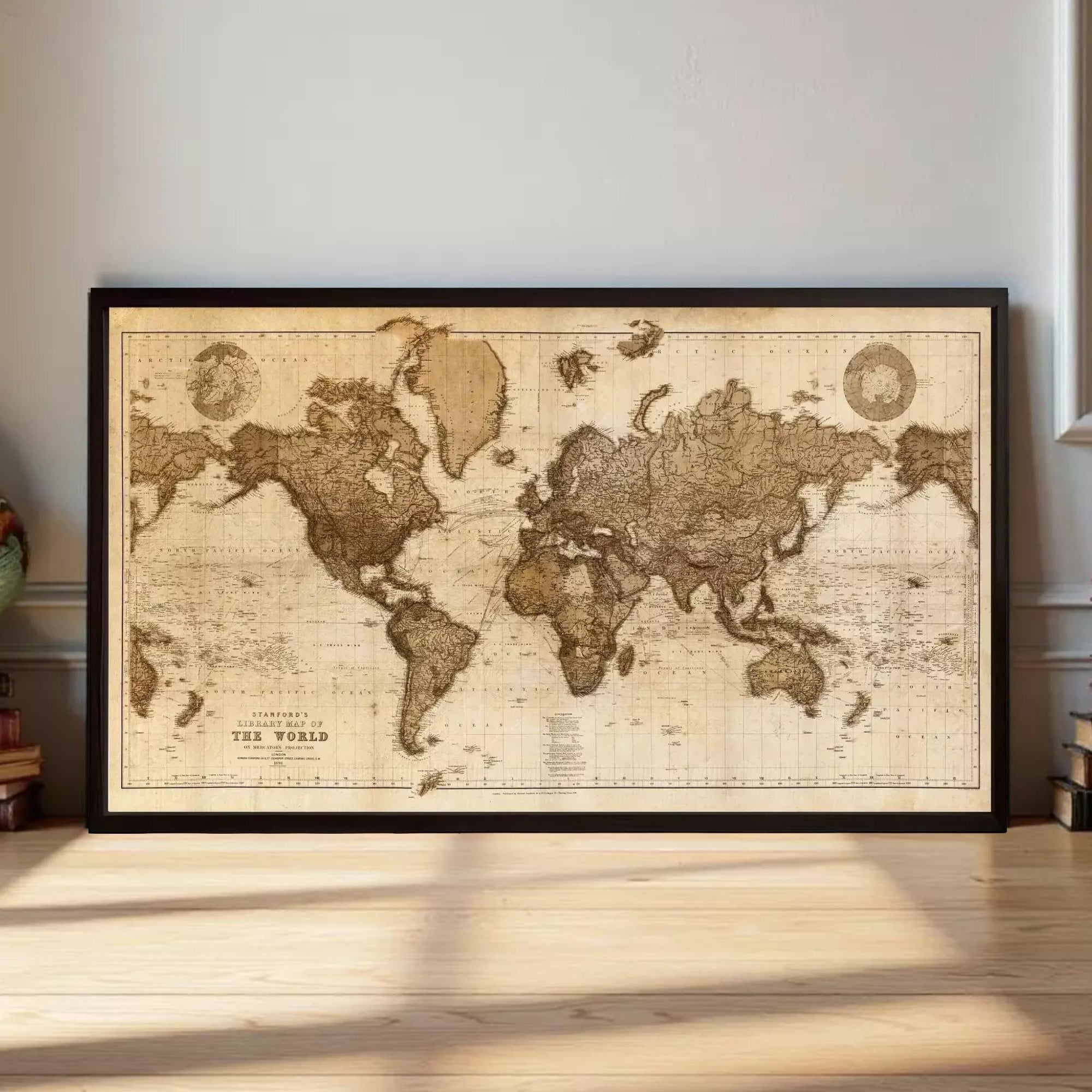 A framed antique world map is displayed on a wooden floor, surrounded by stacks of books and a globe.