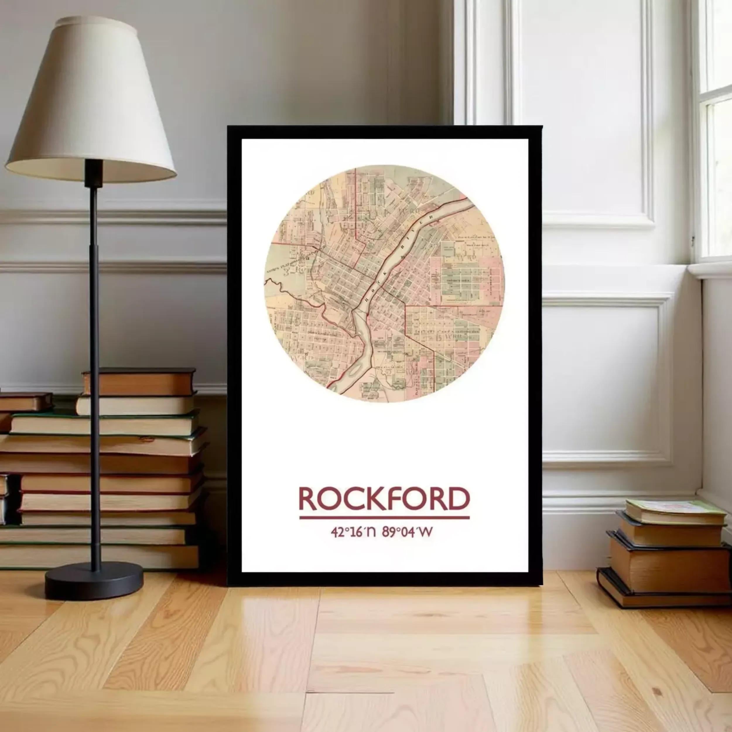 A framed map of Rockford, Illinois, with the text "ROCKFORD 42.16 16.89 W" printed on it, is displayed on a wooden floor next to a stack of books and a lamp.