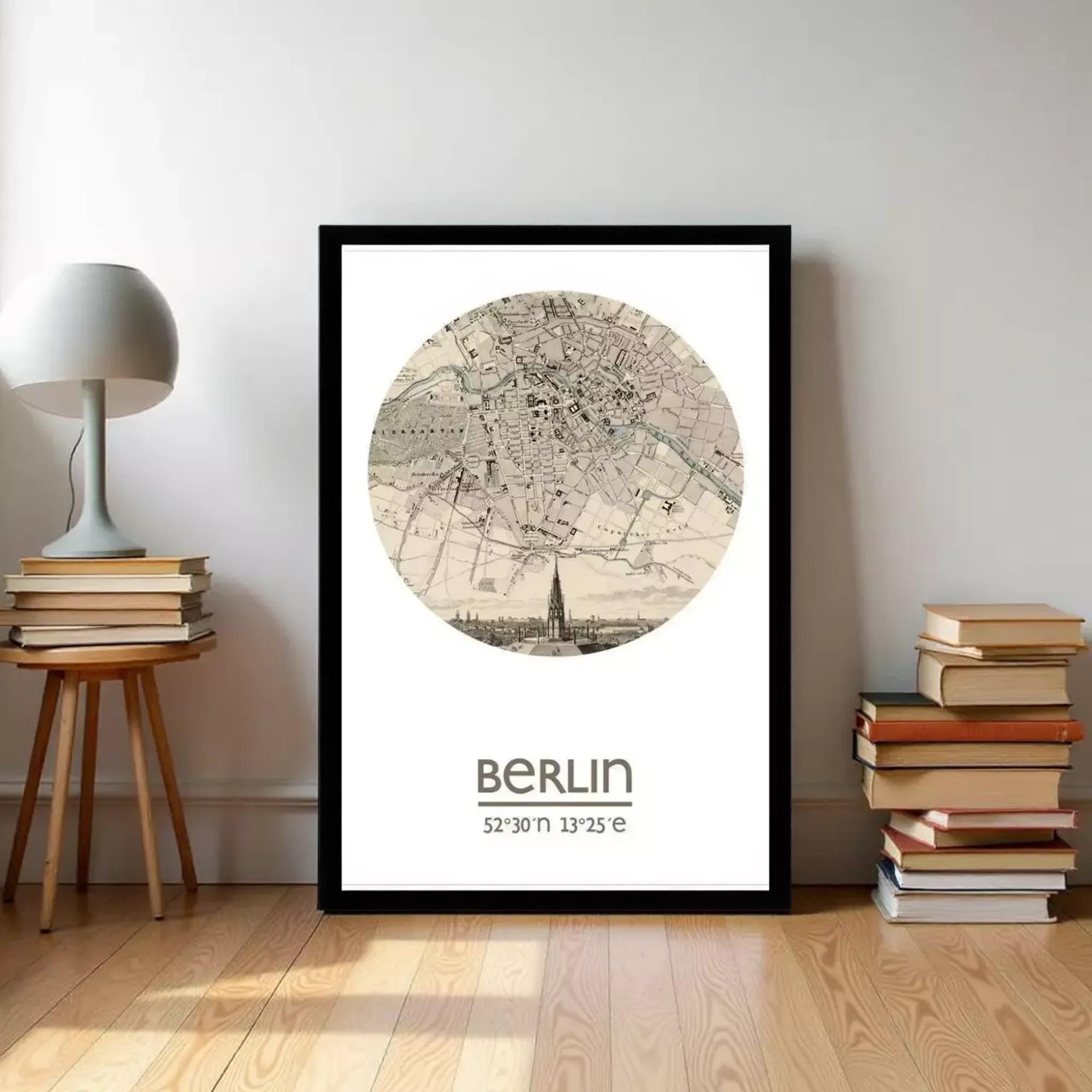 A framed map of Berlin, with a detailed illustration of the city's streets and landmarks, is displayed on a wall in a room with a stack of books and a lamp.