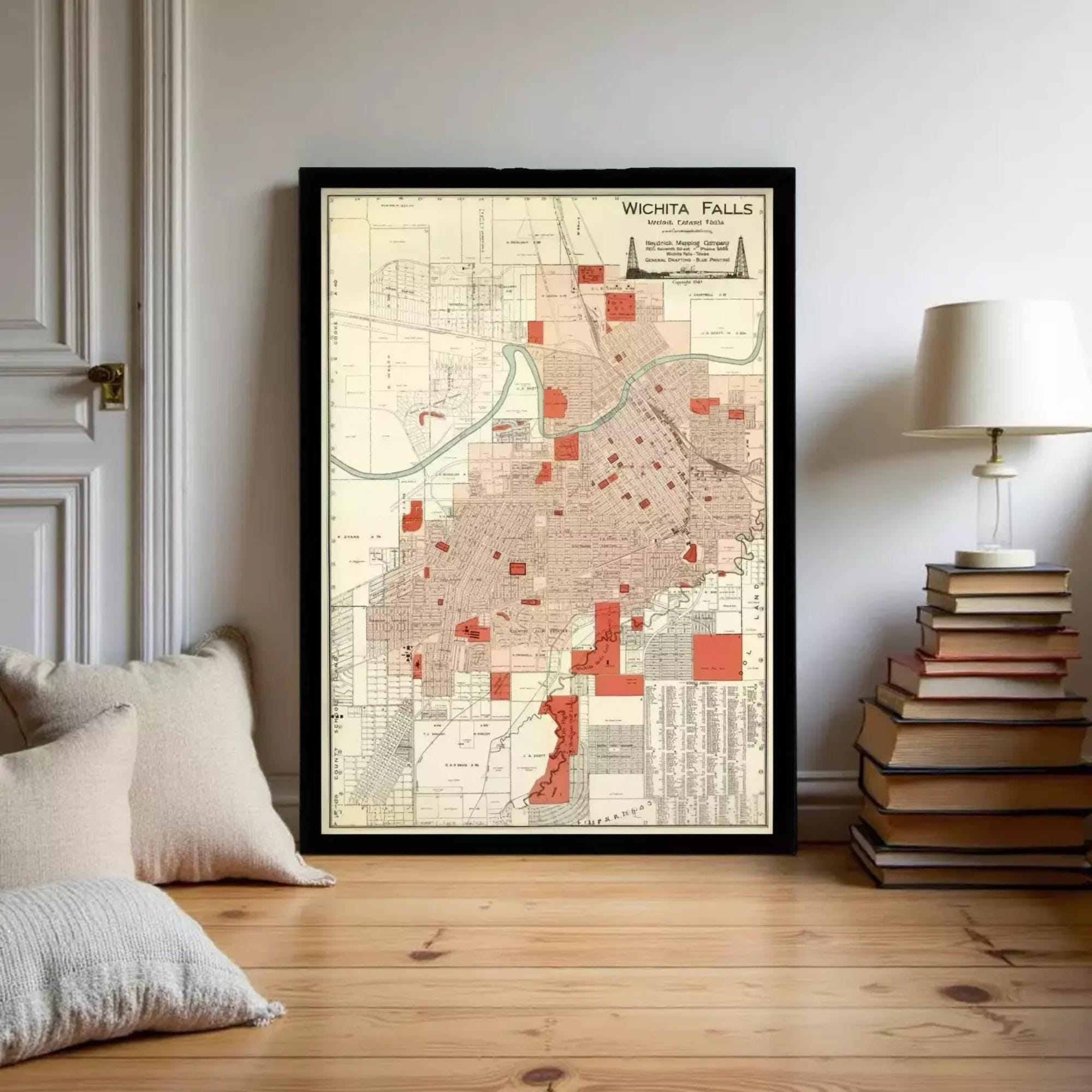 A framed map of Wichita Falls, Texas, displayed on a wall in a room with a stack of books and a lamp.