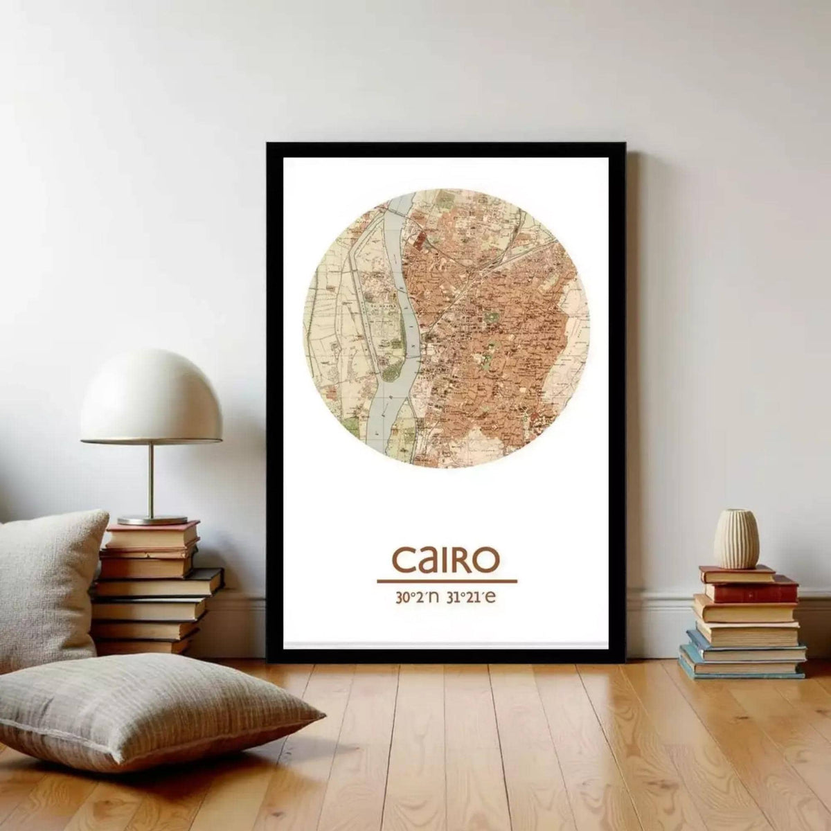 a framed map of Cairo, Egypt, with a stack of books and a lamp on a wooden floor in the foreground.