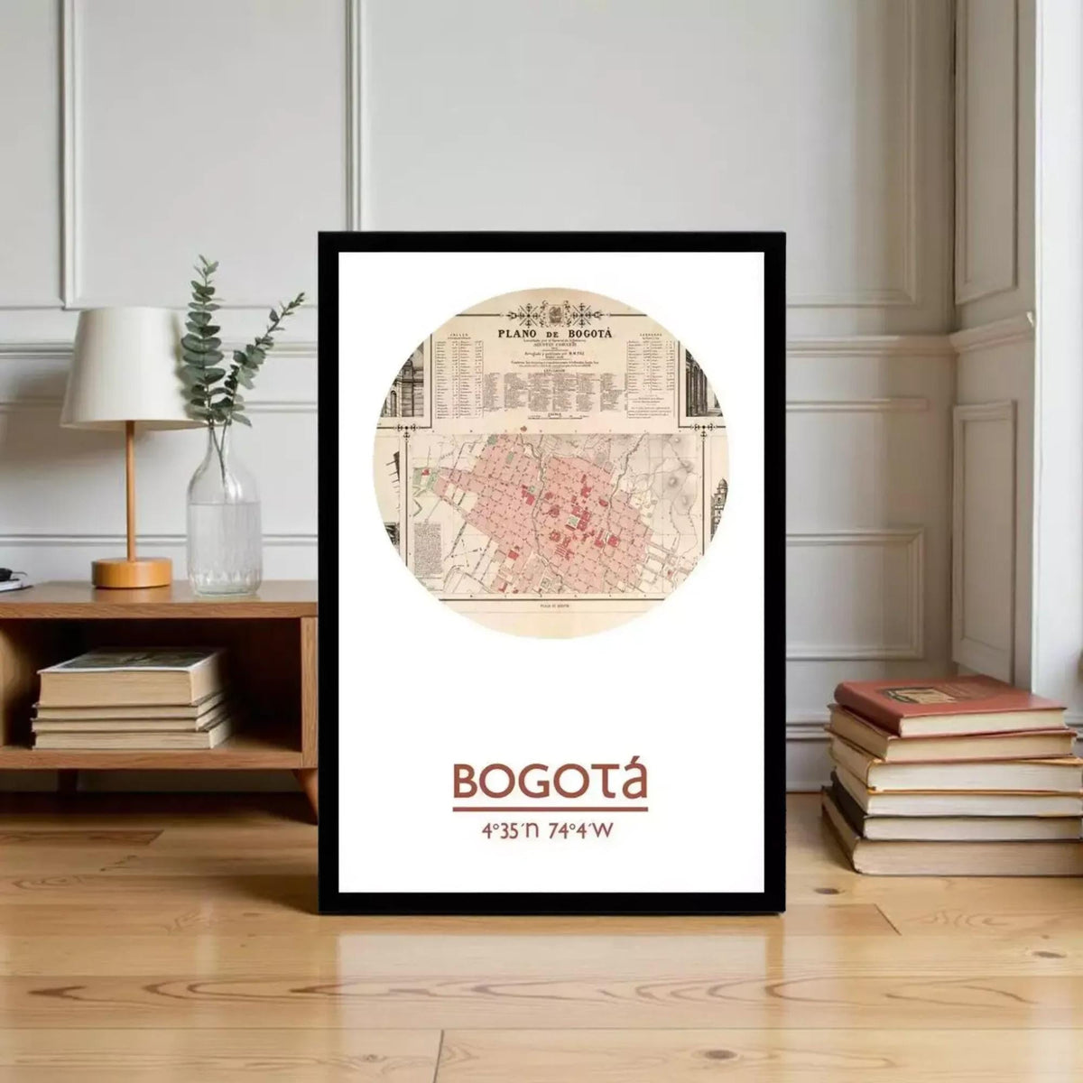 A framed map of Bogota, Colombia, with the text "BOGOTÁ" and a coordinate system, placed on a wooden floor next to a stack of books and a lamp.