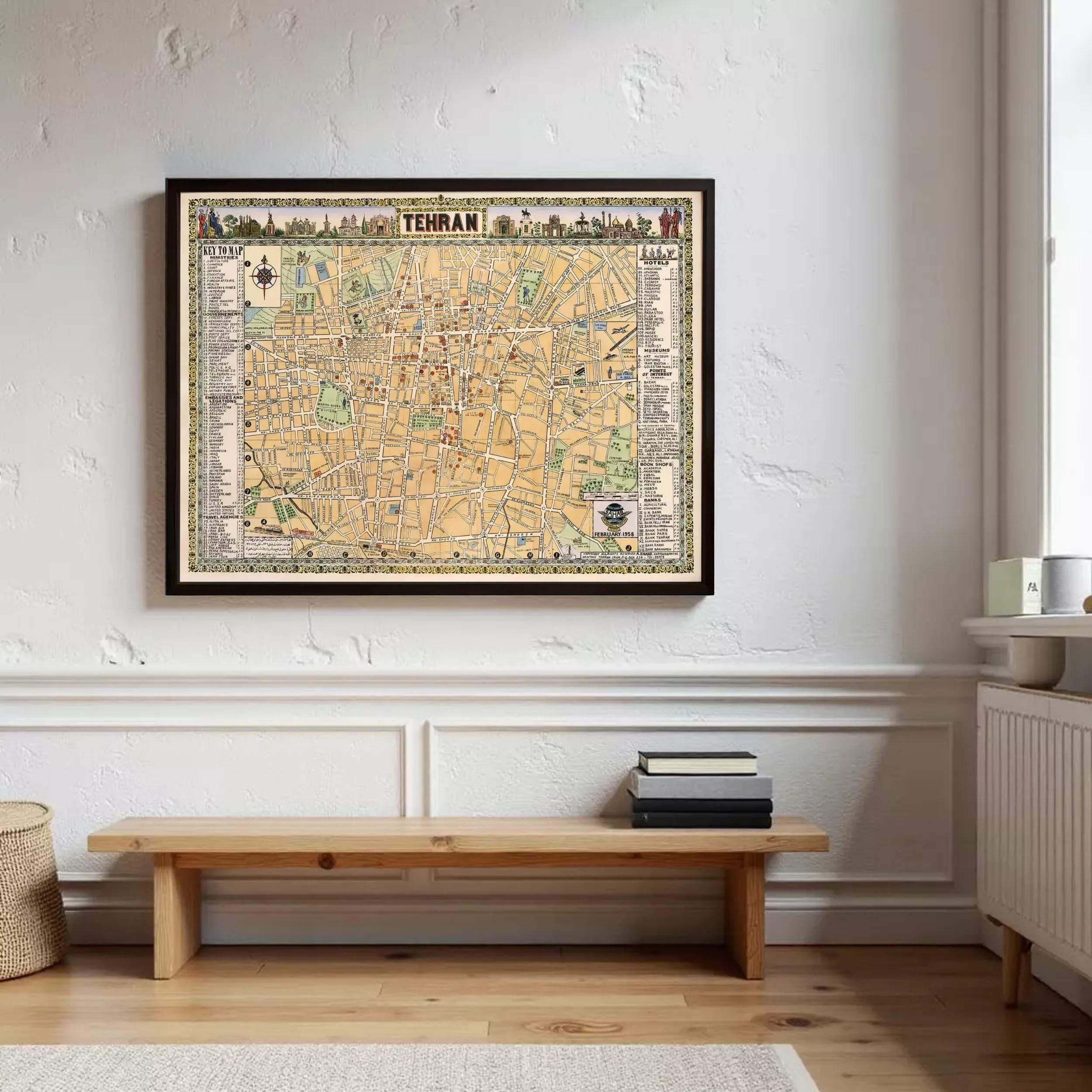 a framed map of Tehran hanging on a wall, with a wooden bench and some books placed in front of it.