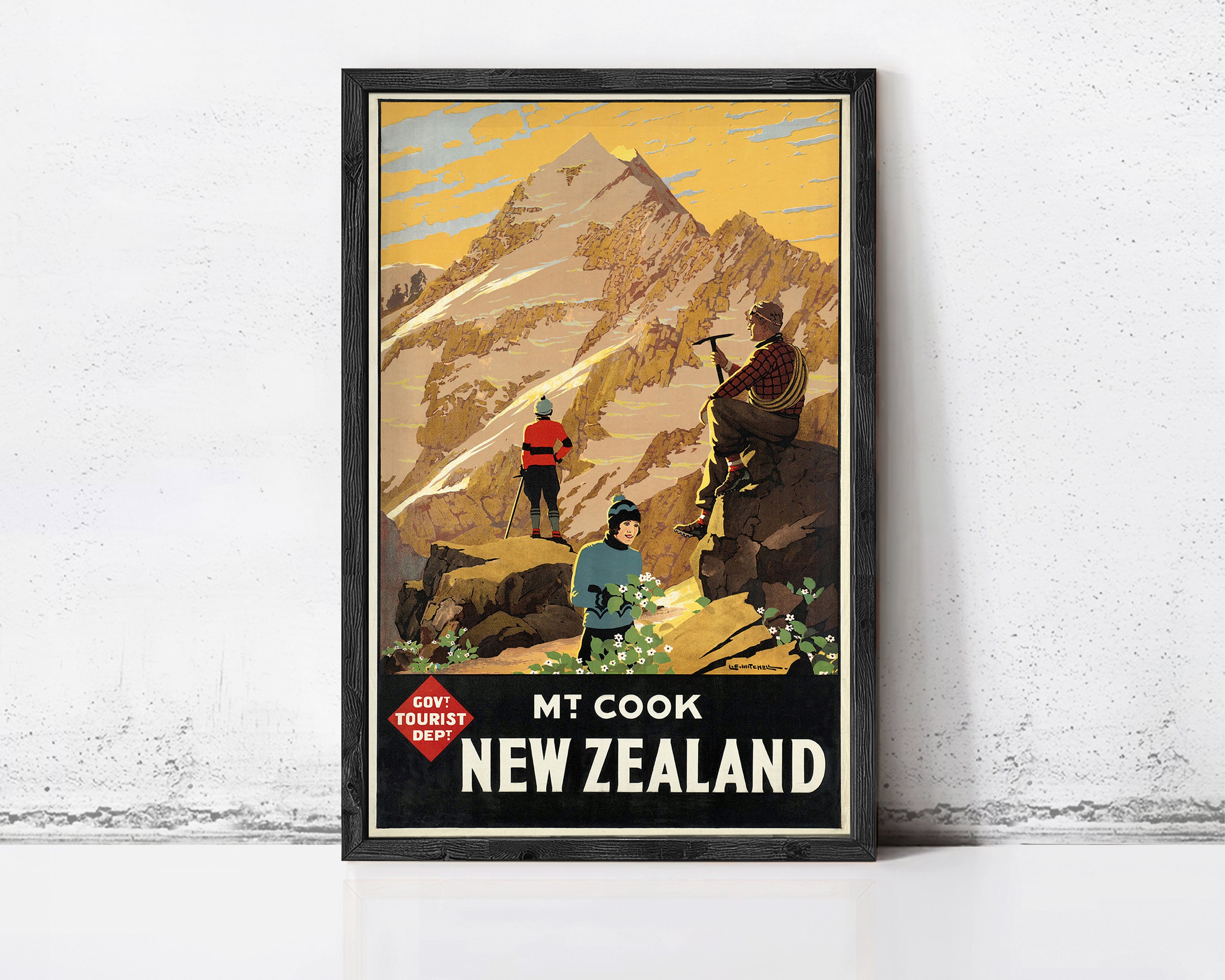 A framed vintage travel poster depicting a mountain landscape with people hiking, set against a yellow sky with clouds.