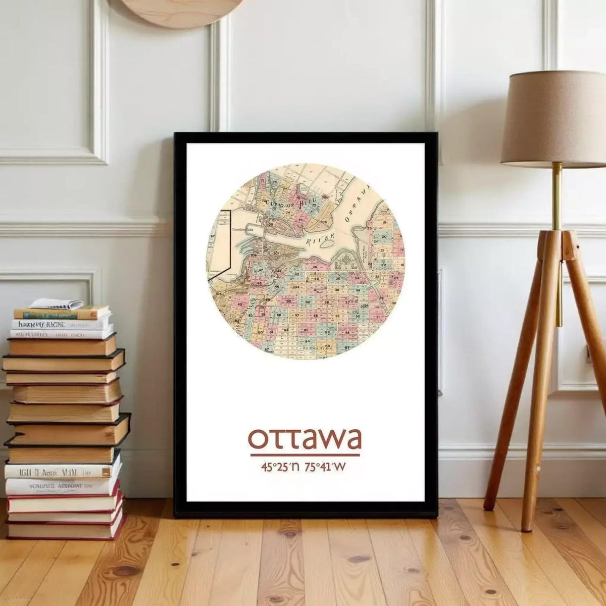 A framed map of Ottawa, Canada, with the city's name and location printed on it, is displayed on a wooden floor next to a stack of books and a lamp.