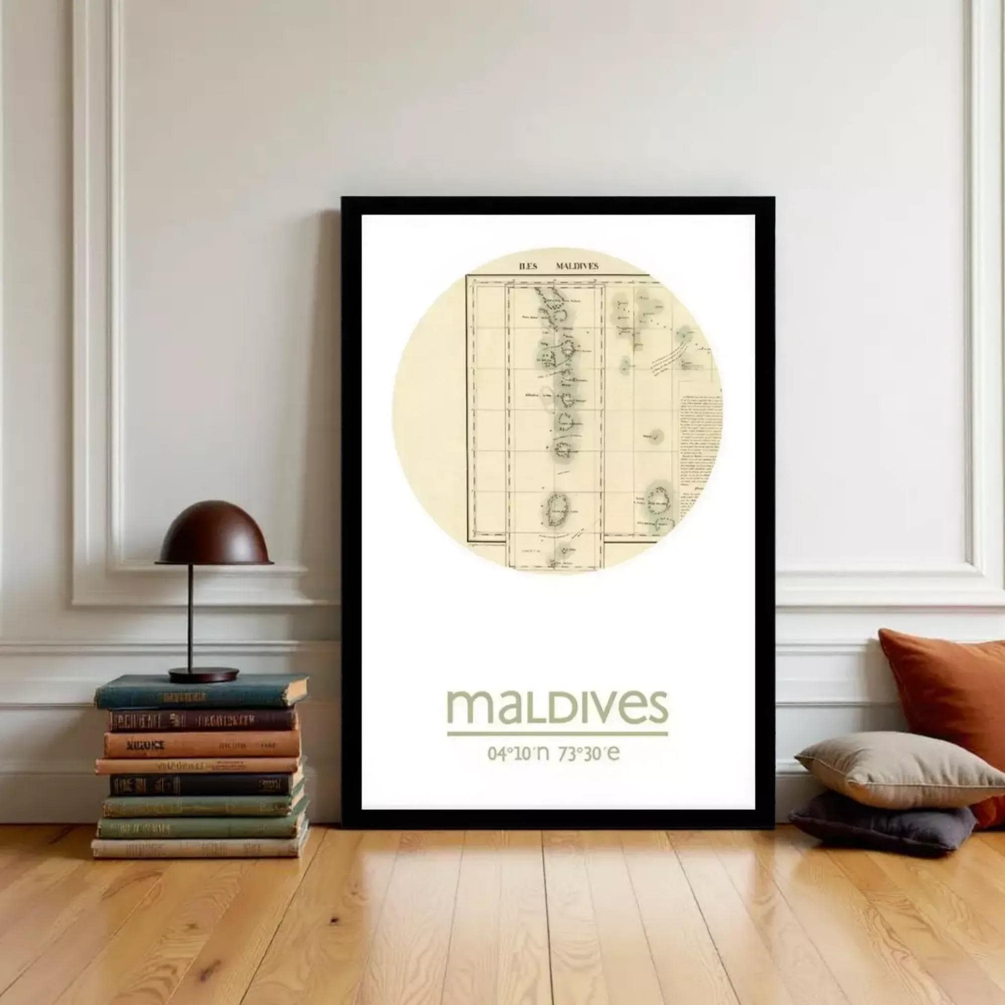A framed poster of the Maldives map is displayed on a wall, with a stack of books and a lamp to the left.