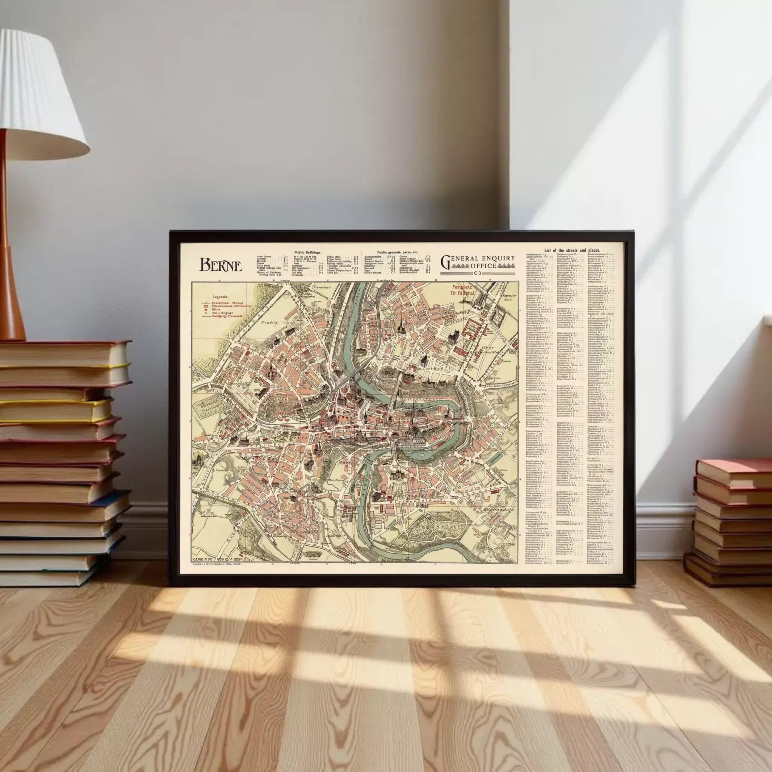 A framed map of the city of Berne, France, displayed on a wooden floor in a room with a lamp and books.