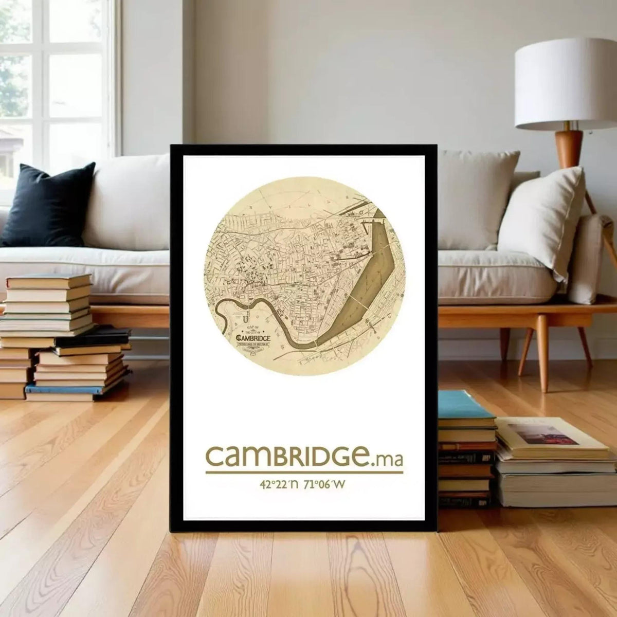 A framed map of Cambridge, England, with the text "Cambridge.ma" and the coordinates "42.22 N 71.96 W" displayed on it, placed on a wooden floor in front of a bookshelf.
