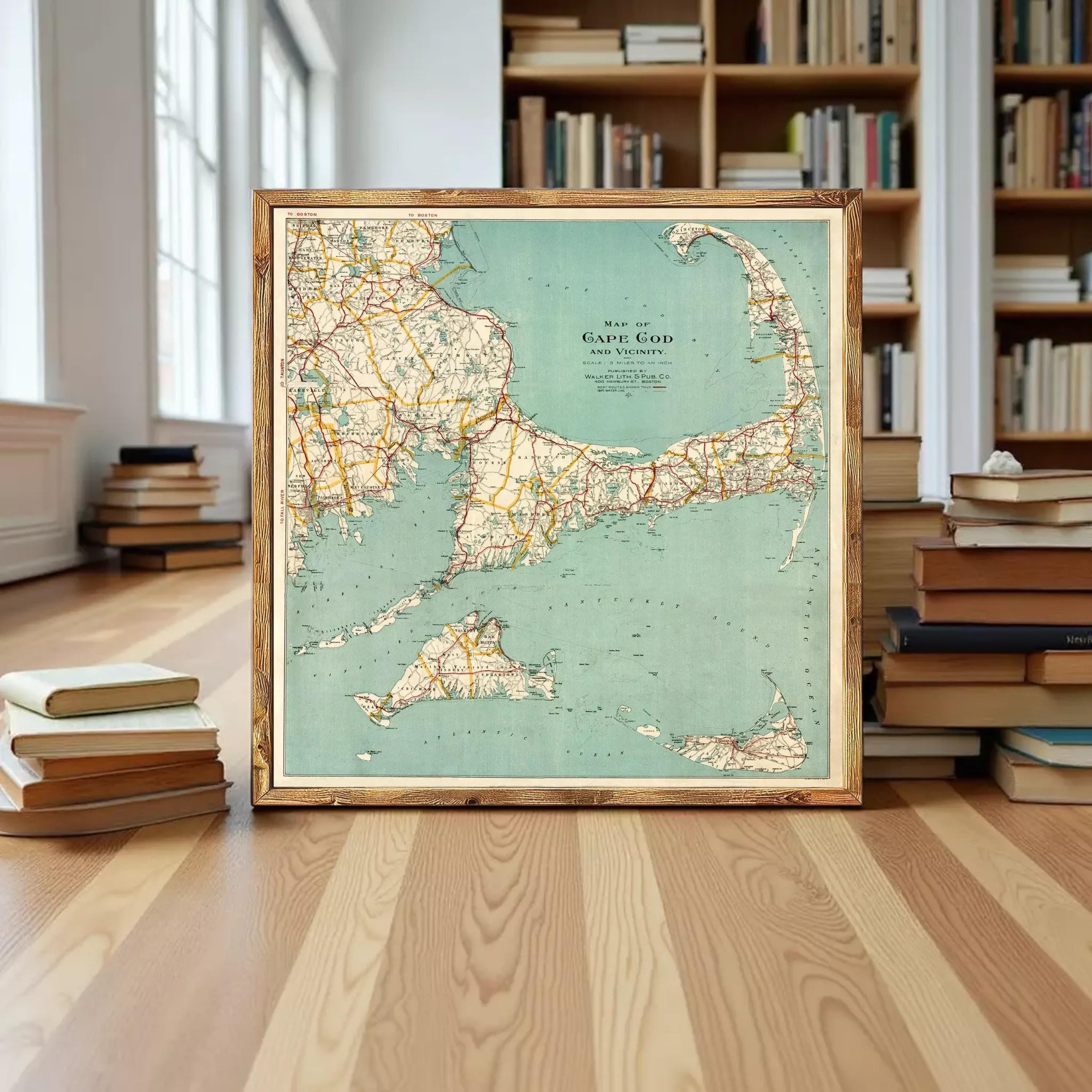 A framed map of Cape Cod, Massachusetts, displayed on a wooden floor in front of a bookshelf filled with books.