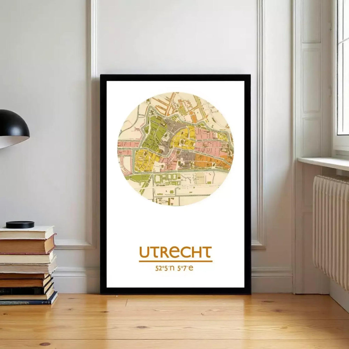 A framed map of Urecht, a city in Germany, is displayed on a wall in a room with a stack of books and a radiator.