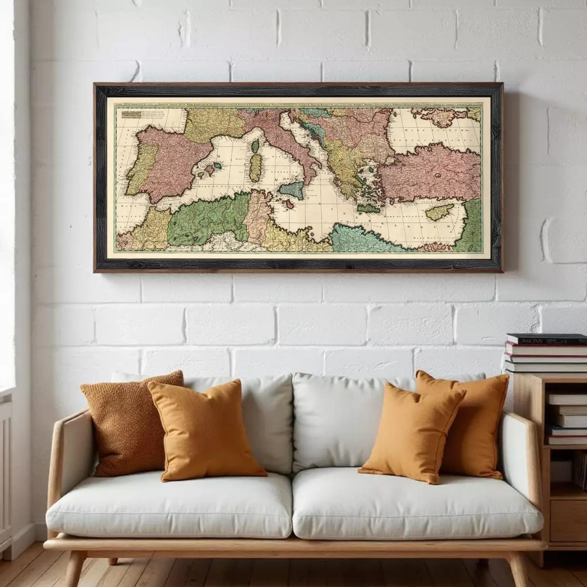A framed vintage map of Europe and the Mediterranean region hangs on a white brick wall above a white couch with orange throw pillows.