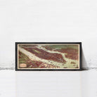The image is a framed painting or map of a city, depicting a densely populated urban area with various buildings, roads, and waterways.