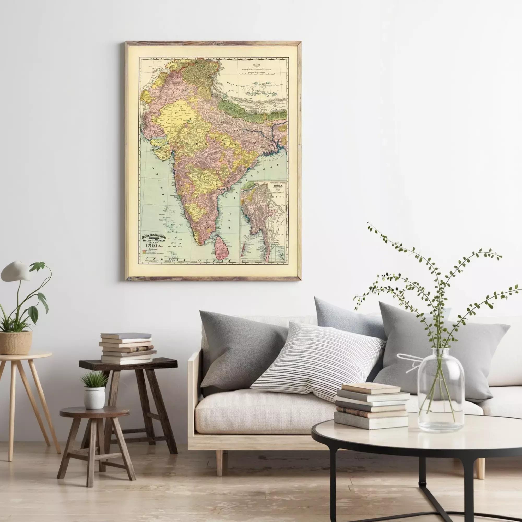 a living room with a large framed map of India hanging on the wall above a couch with pillows. The room also includes a coffee table with books and a vase with greenery.