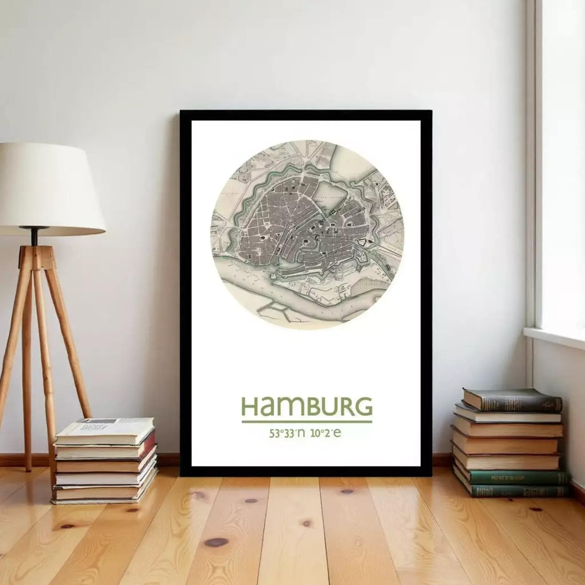 A framed map of Hamburg, Germany, with the text "HAMBURG" and "53.33° 10.2°" printed on it, is displayed on a wall in a room with a lamp and books.