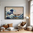 The image is a framed print of the famous Japanese woodblock print "The Great Wave off Kanagawa" by the artist Hokusai. The print depicts a large, powerful wave crashing against a rocky shore, with the wave's crest towering over the surrounding landscape. The artwork is framed in a black frame and is displayed on a white wall.
