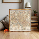 a framed map of Budapest, a city in Hungary, placed on a wooden floor in a room with a lamp and books.