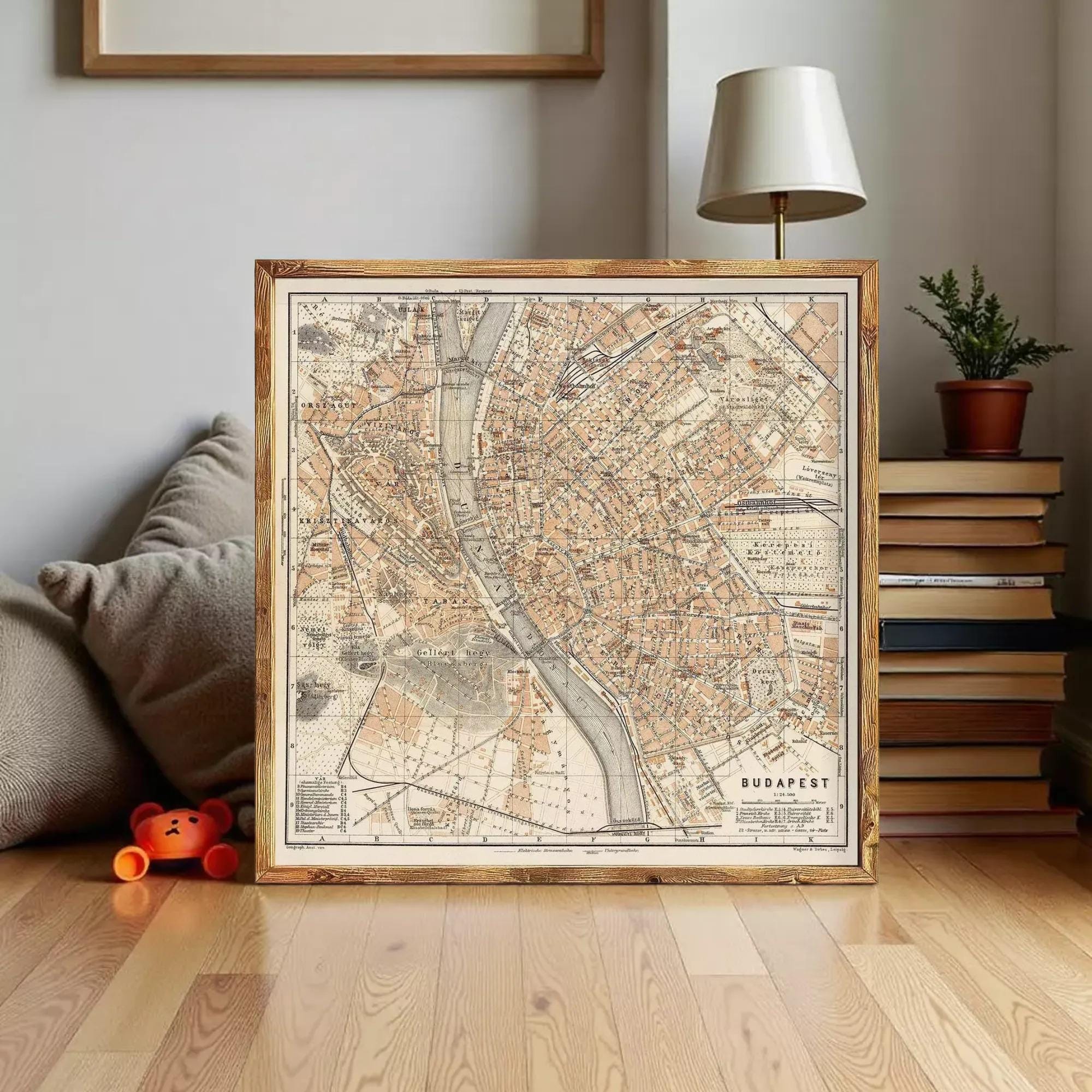 a framed map of Budapest, a city in Hungary, placed on a wooden floor in a room with a lamp and books.